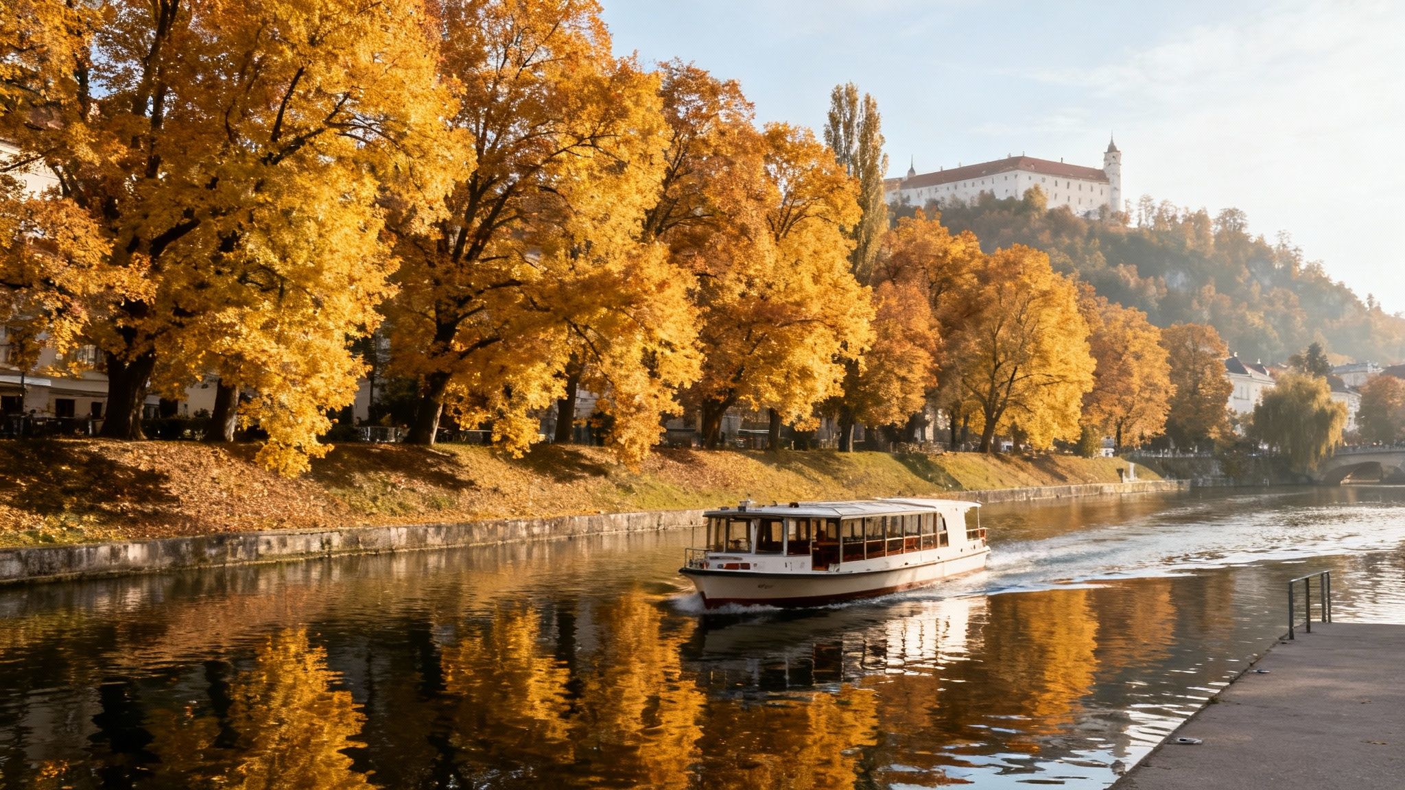 Tourist boat cruising along river lined with golden autumn trees and historic castle on hillside