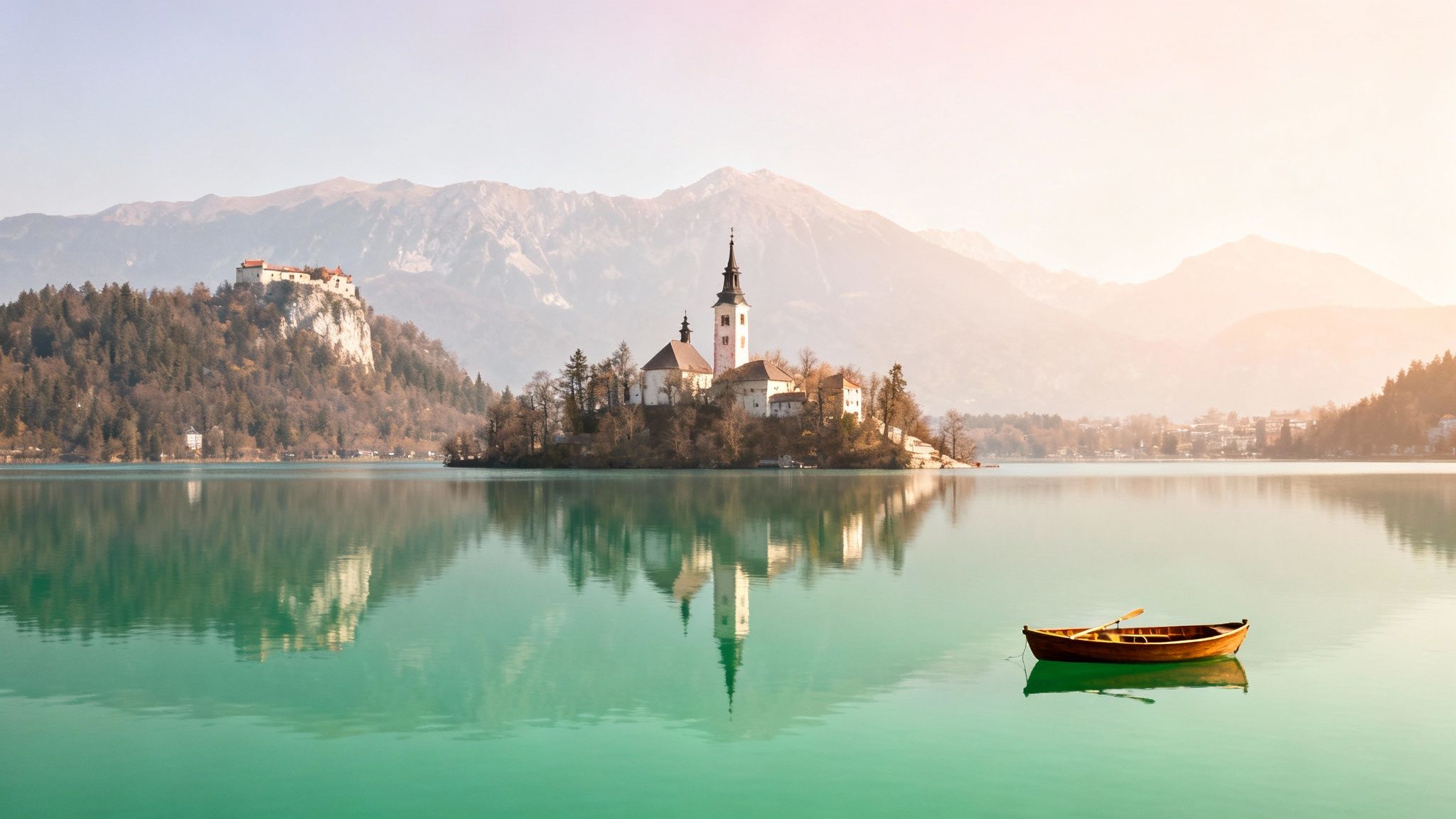 Scenic view of Lake Bled with its iconic island church, a castle, and a wooden boat.
