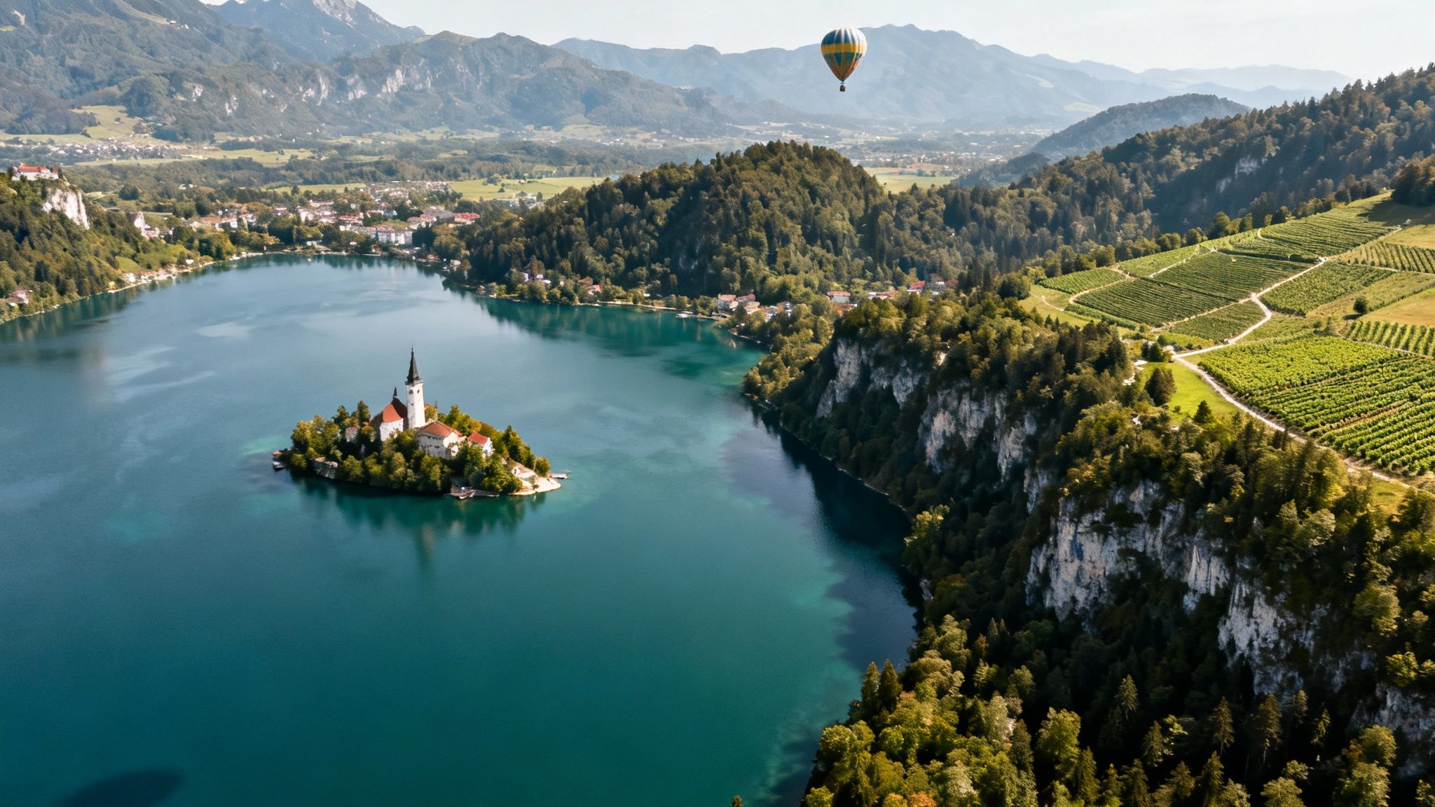 Stunning aerial view of Lake Bled, Slovenia, with island church, a hot air balloon, mountains, and vineyards.