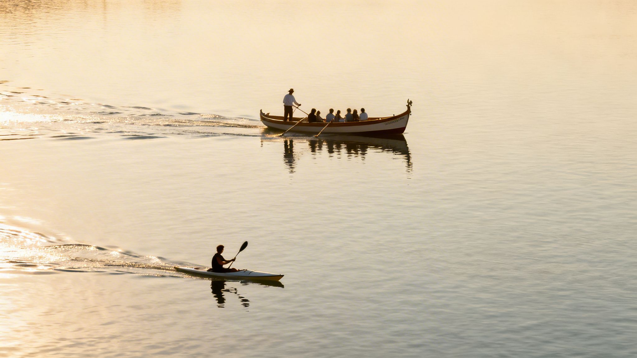 A traditional rowboat with passengers and a solo kayaker navigate sunlit golden water.