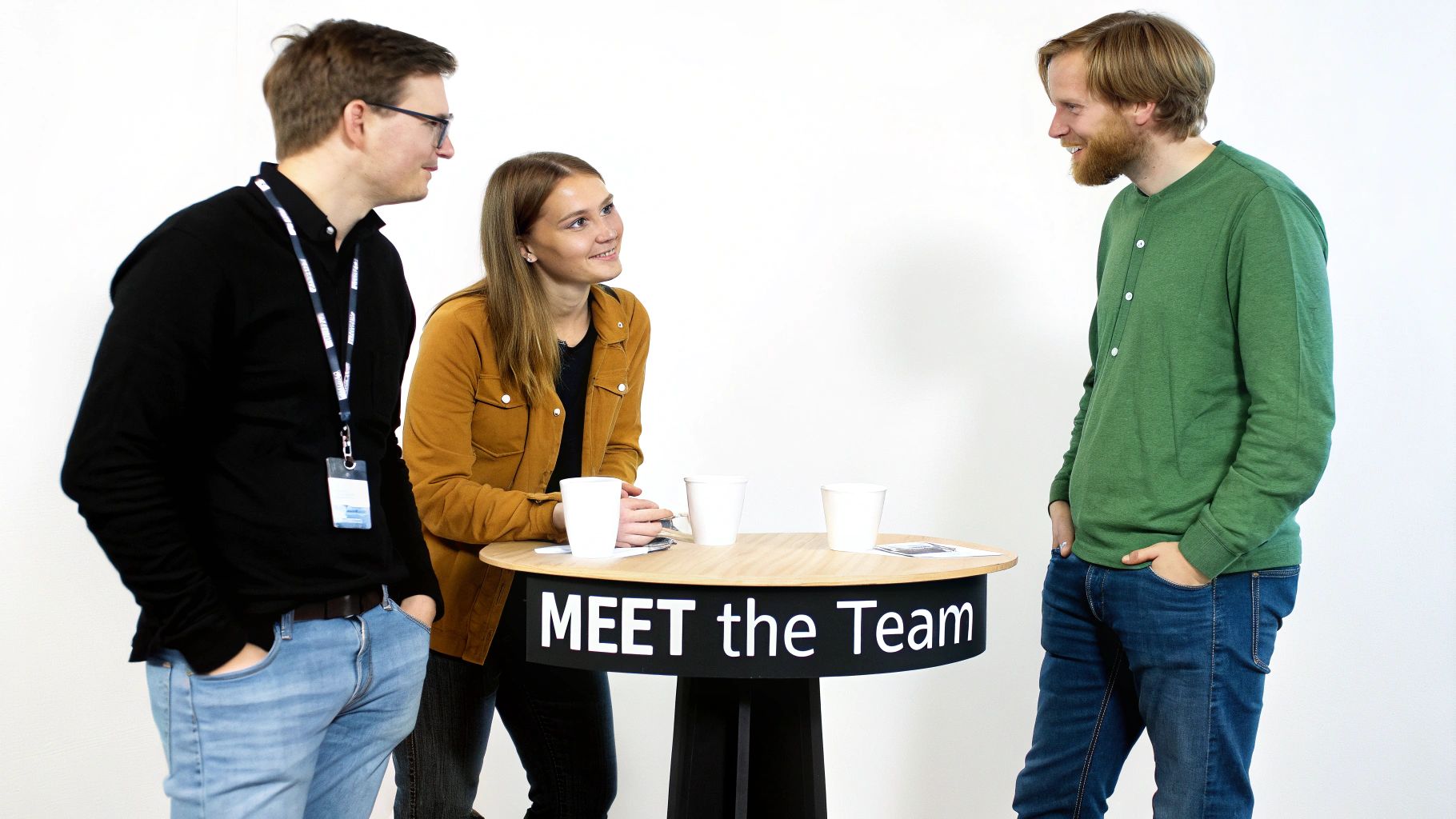 Three young professionals, two men and a woman, networking around a 'MEET the Team' table.