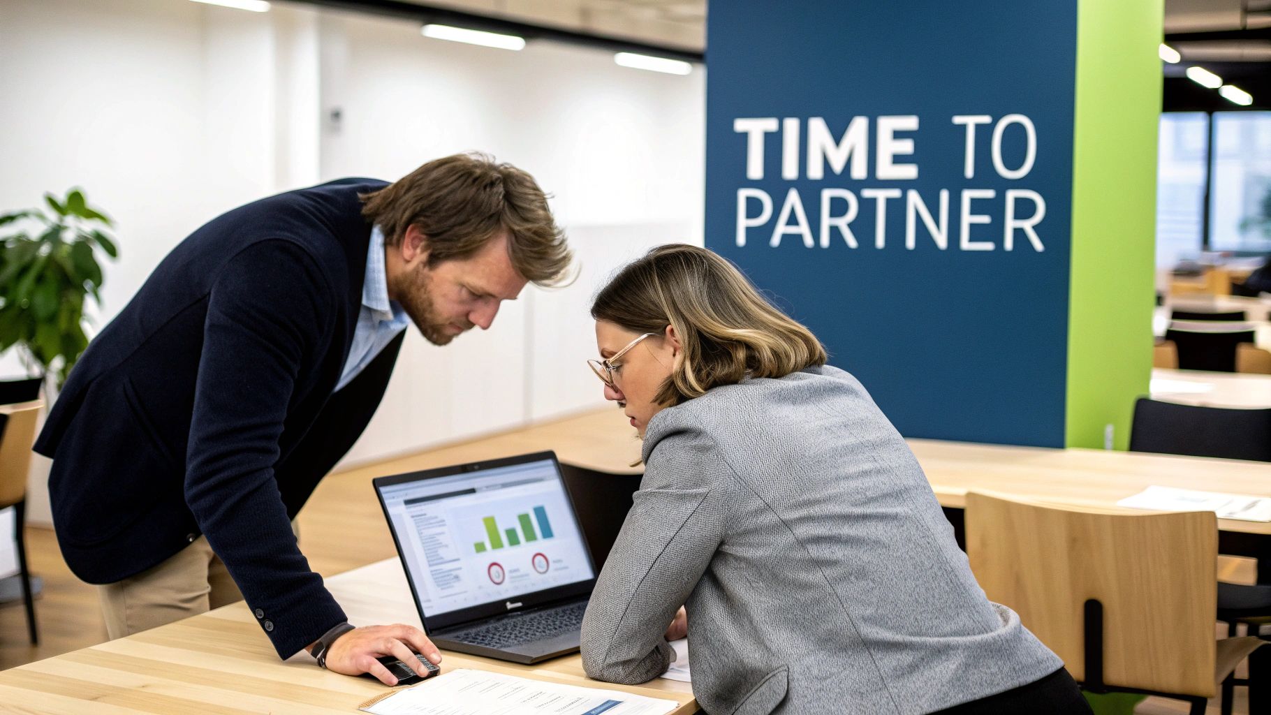 Two business professionals analyze data on a laptop in an office setting, collaborating on a project.