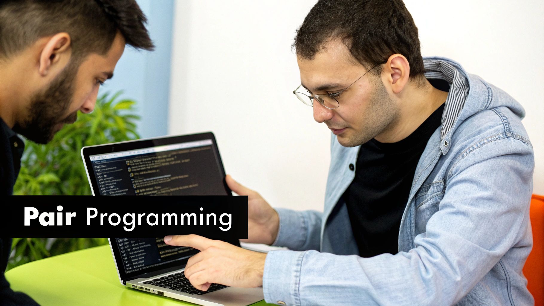 Two developers collaboratively working on a laptop, pointing at code on the screen, demonstrating pair programming.