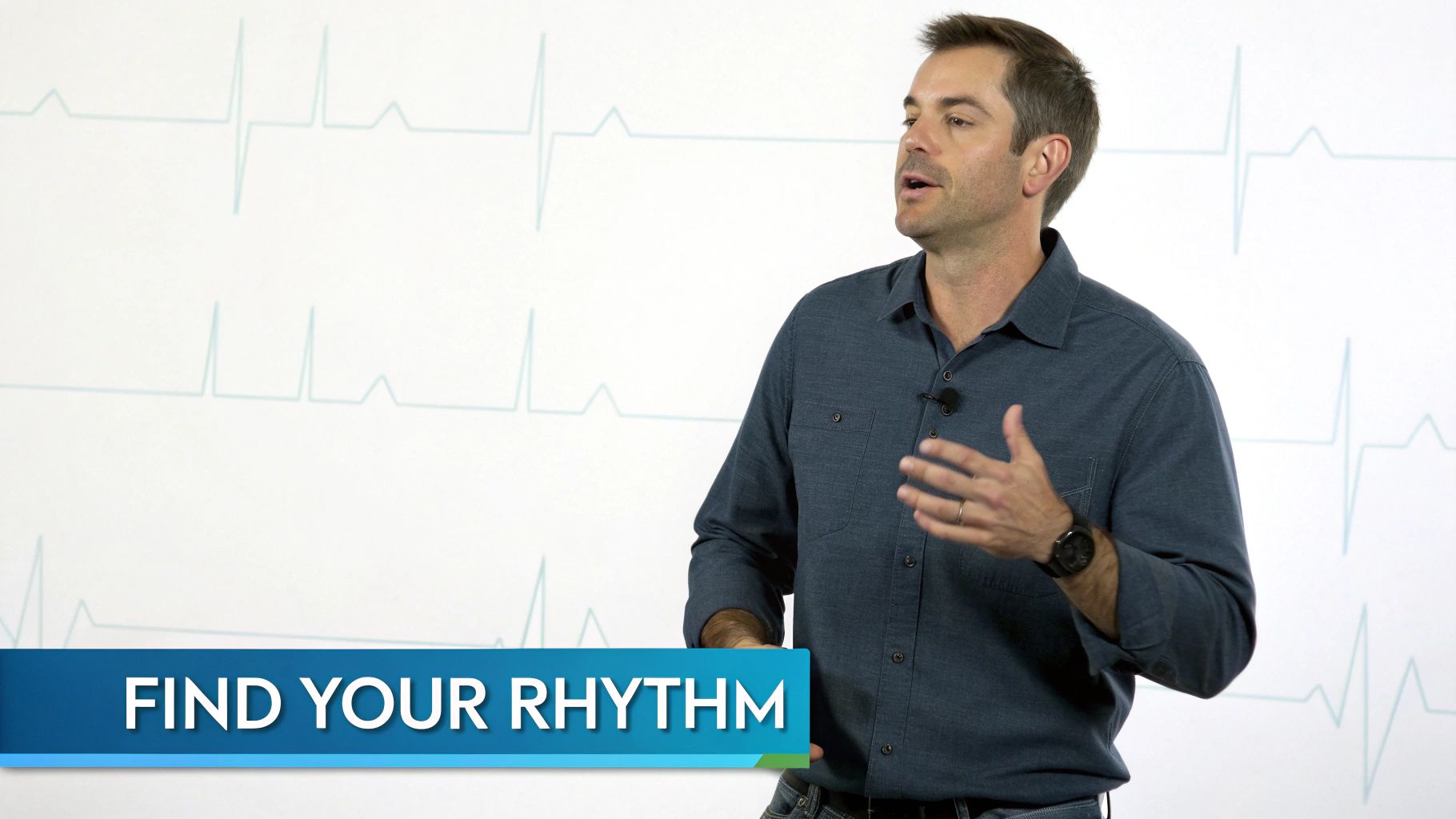 A man in a blue shirt speaks passionately, gesturing, with an ECG background and 'FIND YOUR RHYTHM' text.