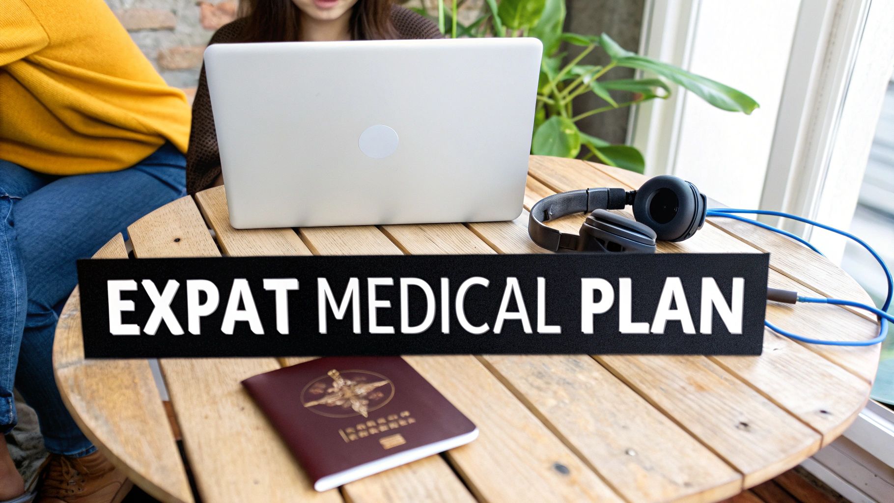 Two people working on a laptop at a wooden table with a passport, headphones, and 'EXPAT MEDICAL PLAN' text.