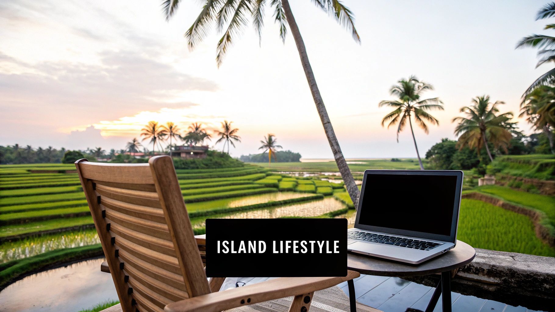 Digital nomad setup with laptop and chair overlooking rice fields and palm trees at sunset.