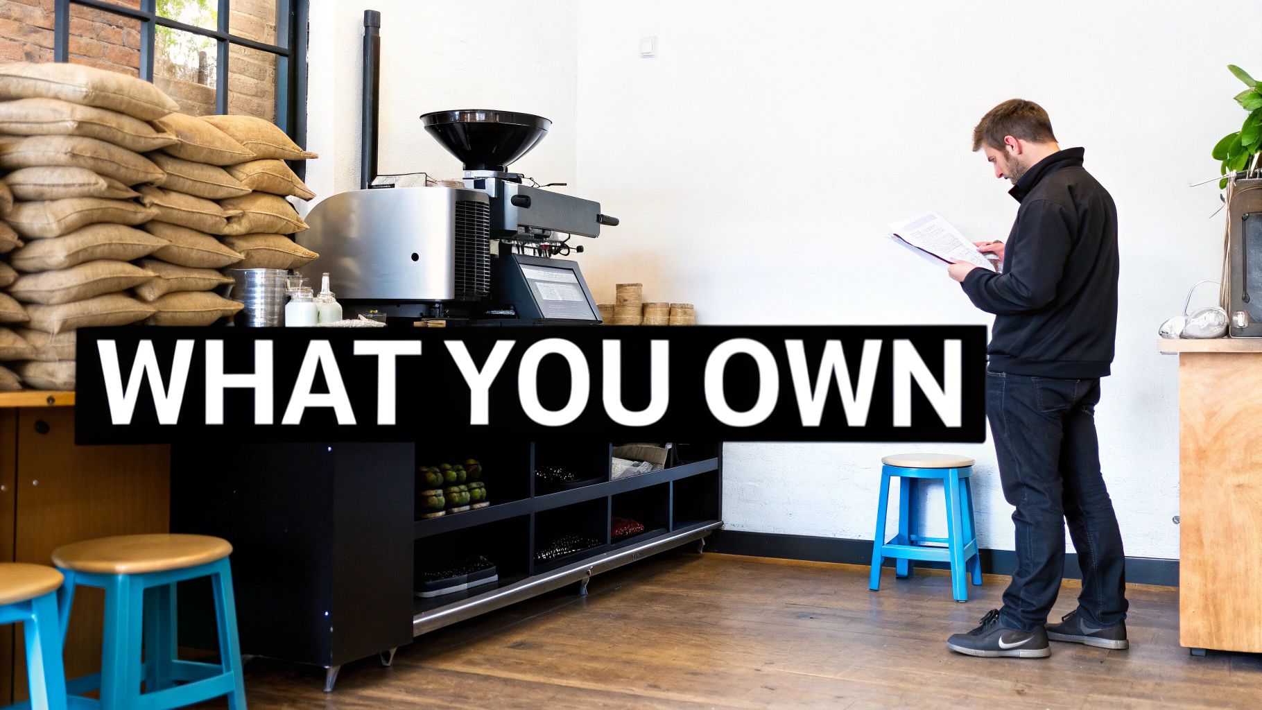 A man reads documents in a modern coffee shop with bags of coffee beans and a roaster.