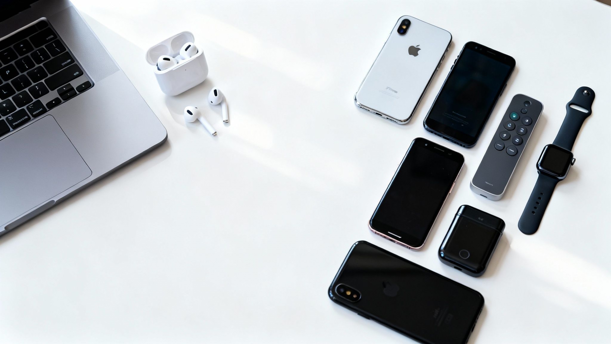 A flat lay of various Apple tech gadgets, including iPhones, AirPods, Apple Watch, and a MacBook.
