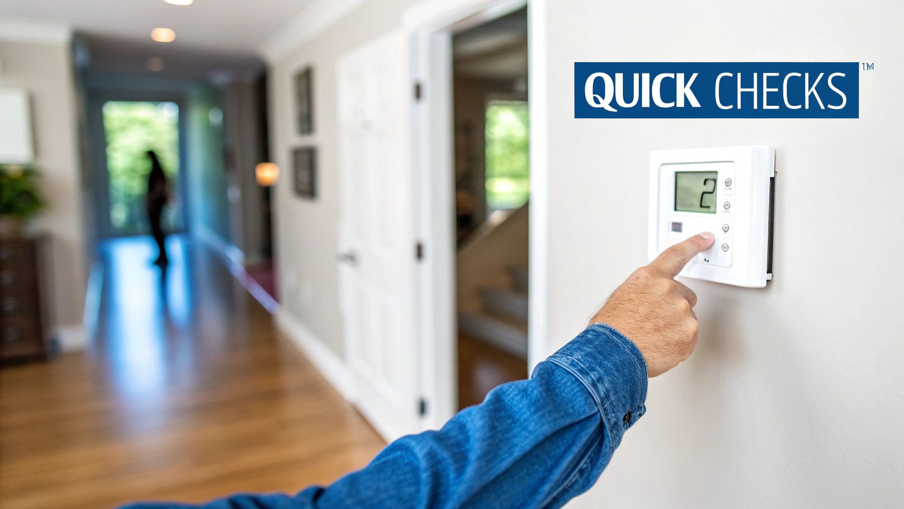 A person adjusts a white digital thermostat on a wall in a bright home hallway.
