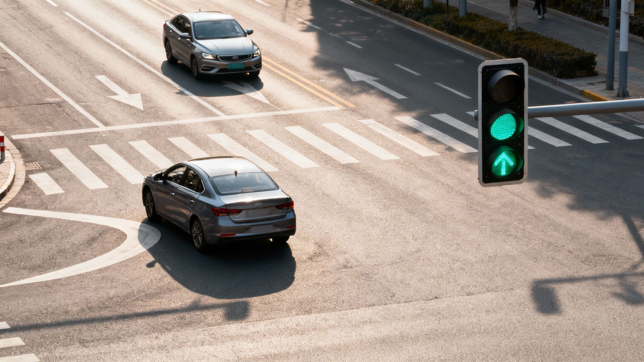 Overhead view of cars at a city intersection with a green traffic light and crosswalk.