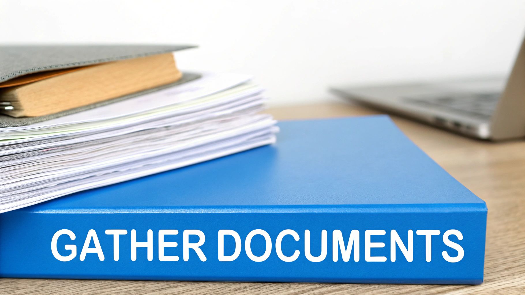 A blue binder labeled 'GATHER DOCUMENTS' on a desk with a stack of papers and a laptop.