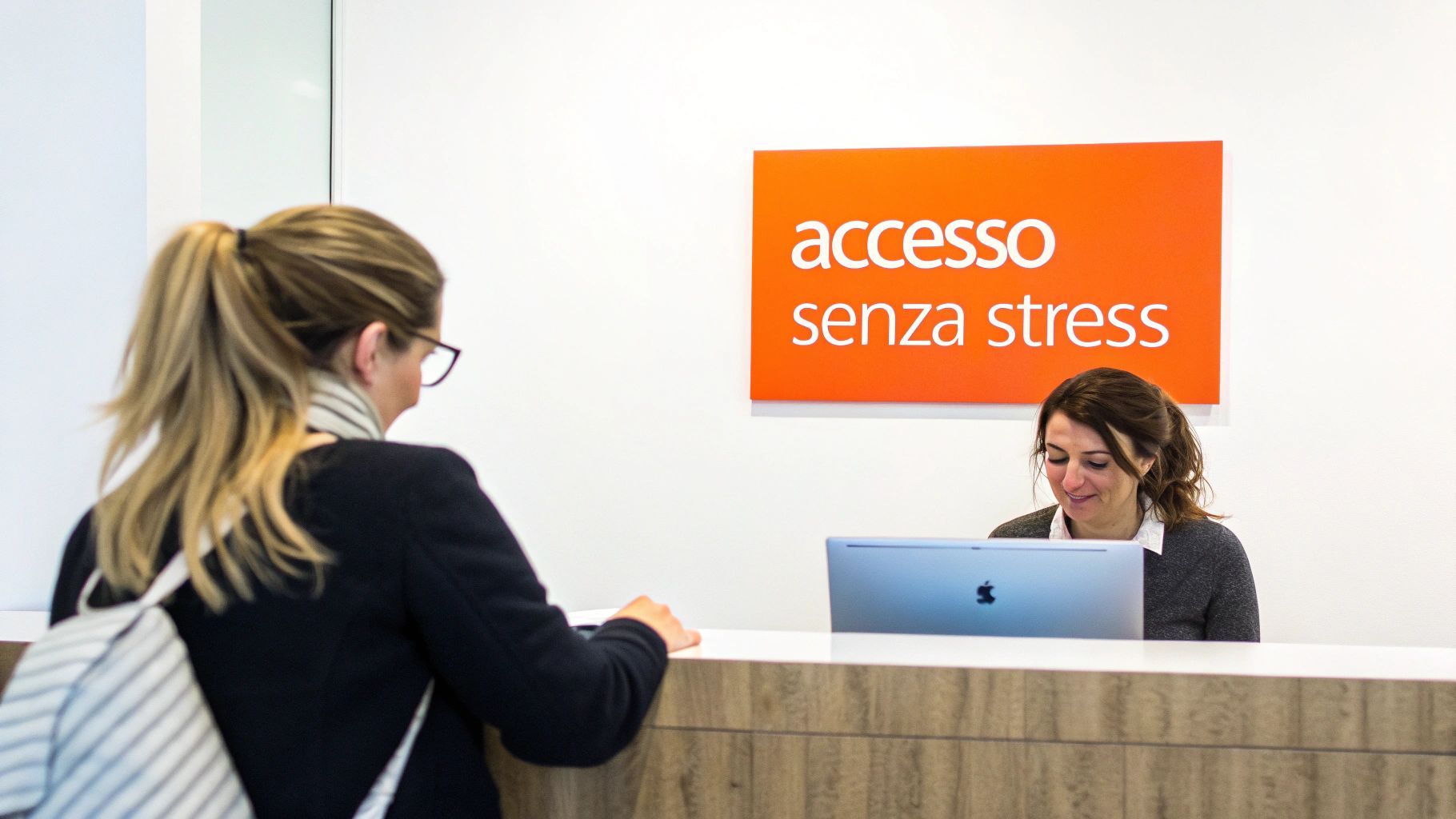 Due donne in una reception: una cliente vista di spalle e una receptionist sorridente al computer sotto il cartello "accesso senza stress".