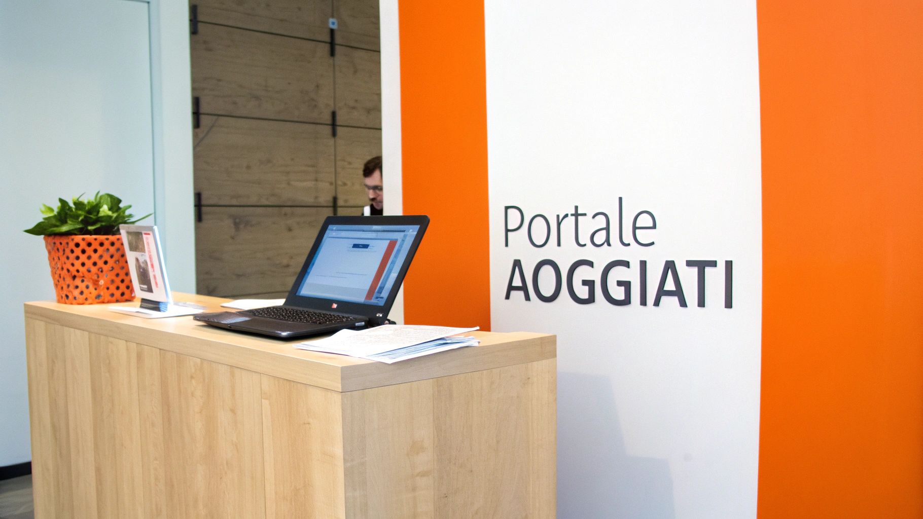 Reception in legno con laptop, pianta in vaso arancione e documenti, sfondo con scritta 'Portale AOGGIATI'.