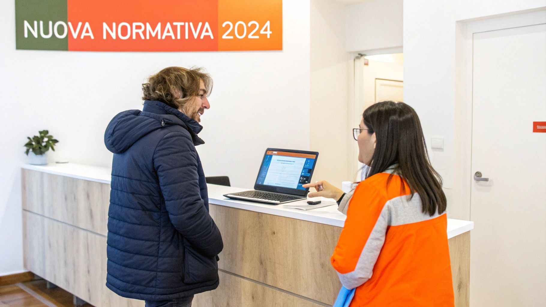 Uomo e donna discutono davanti a un laptop presso una reception con la scritta 'Nuova Normativa 2024'.