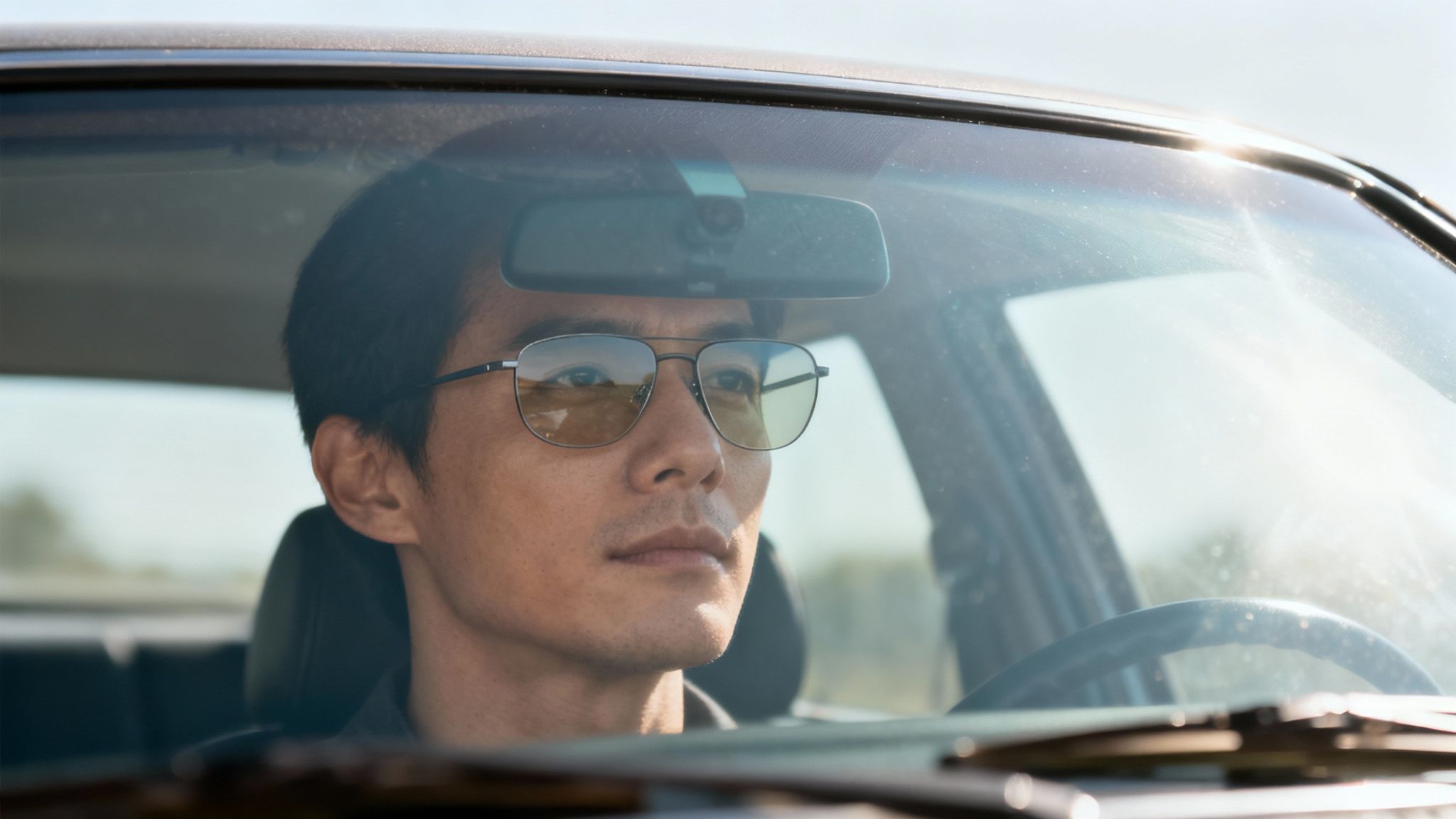 A person driving a car in sunny weather, illustrating the need for sunglasses.