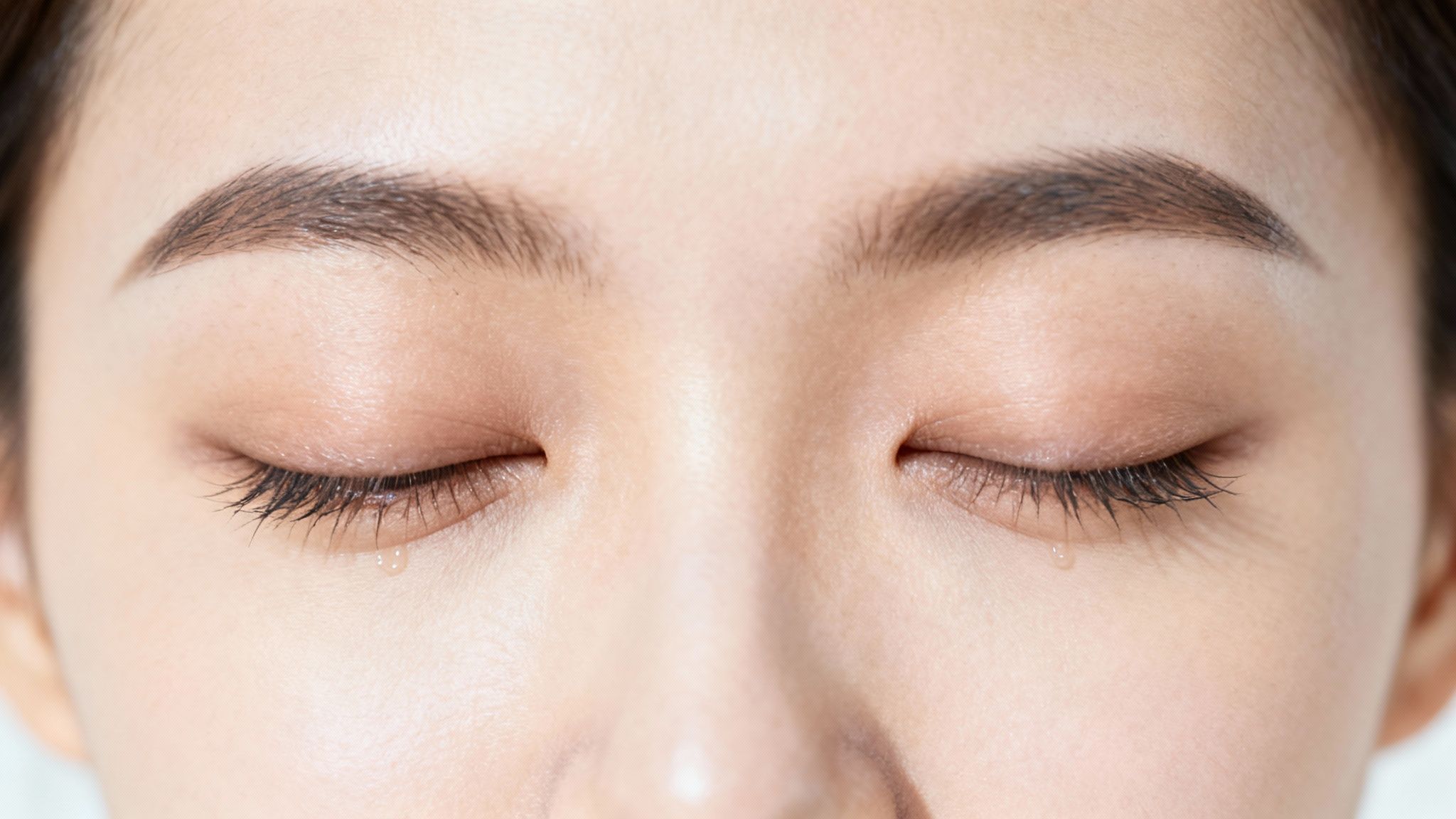 Close-up of a person's closed eyes with tears dripping, suggesting sadness or discomfort.