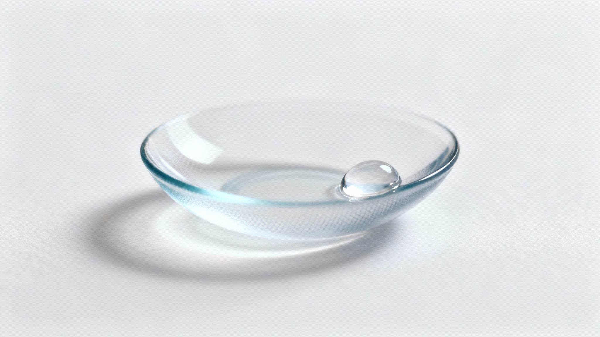 Clear contact lens resting on clean white surface with water droplet nearby