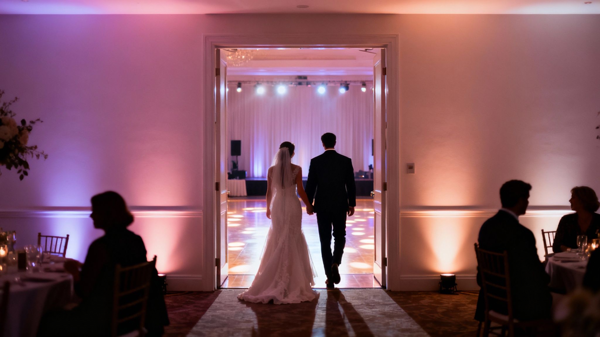 Bride and groom holding hands, walking into a wedding reception illuminated with colorful ambient lighting.