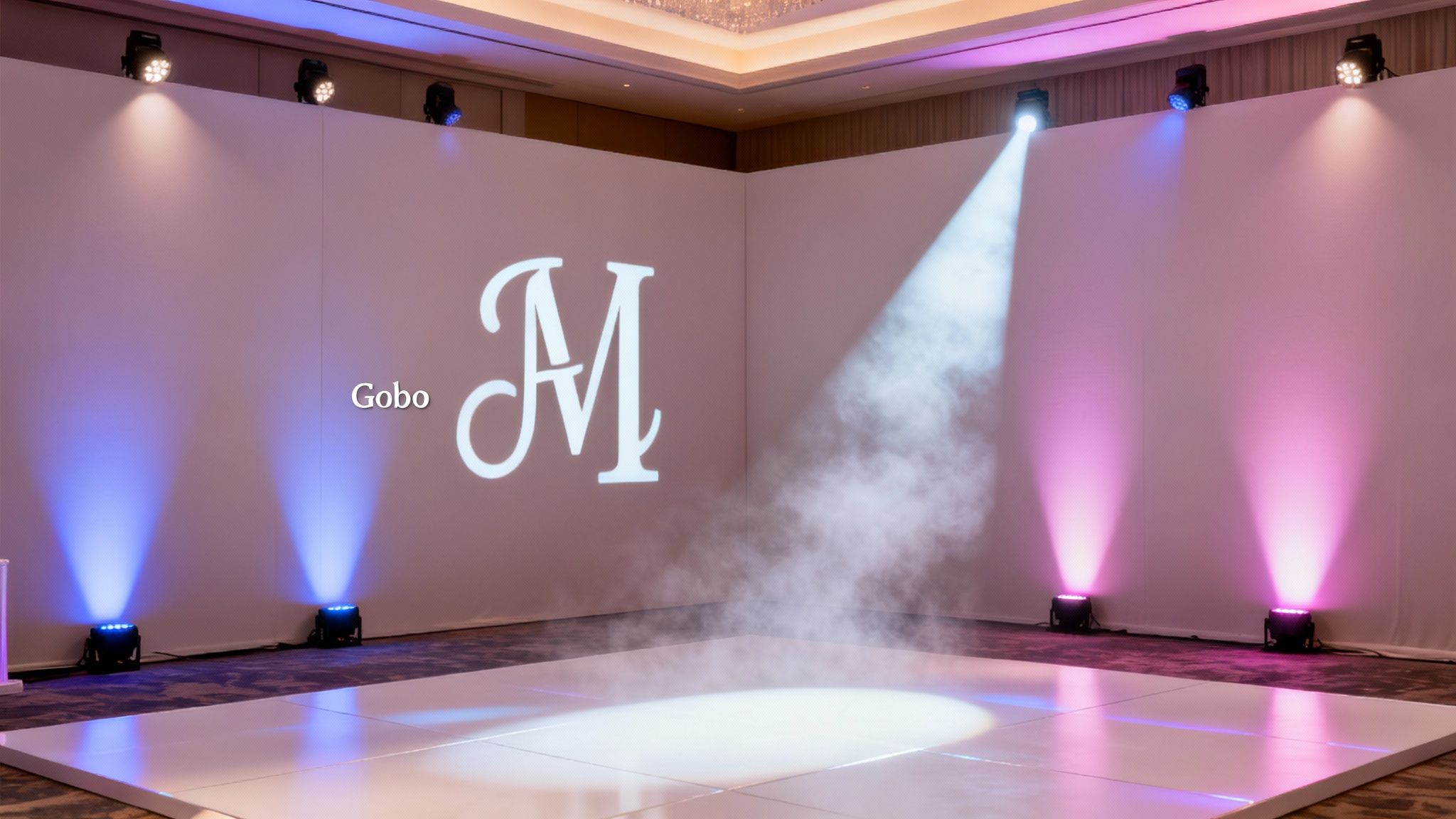 Elegant event setup with white dance floor, backdrop, projected monogram, and colorful stage lighting with haze.