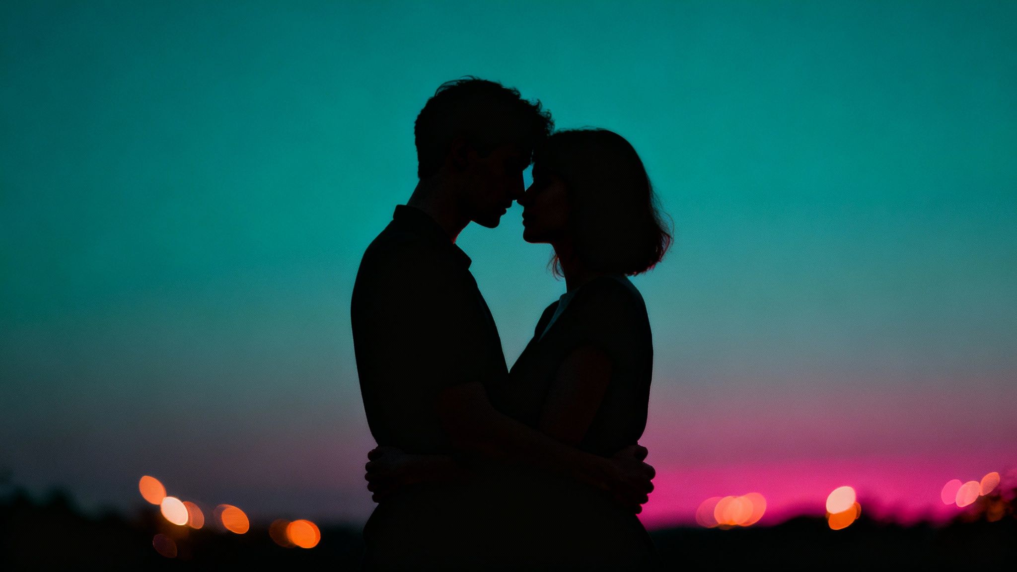 Romantic couple silhouette touching foreheads at sunset with bokeh city lights background