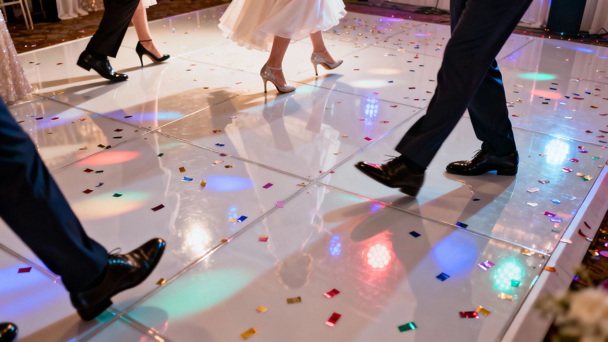 People's feet dancing on a light-up floor scattered with colorful confetti at a reception.