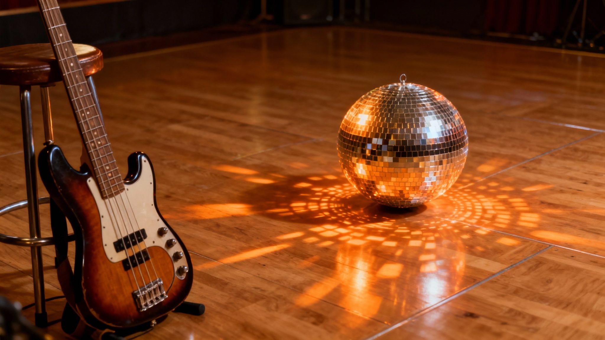 A bass guitar leaning against a stool on a wooden floor, next to a sparkling disco ball casting light patterns.