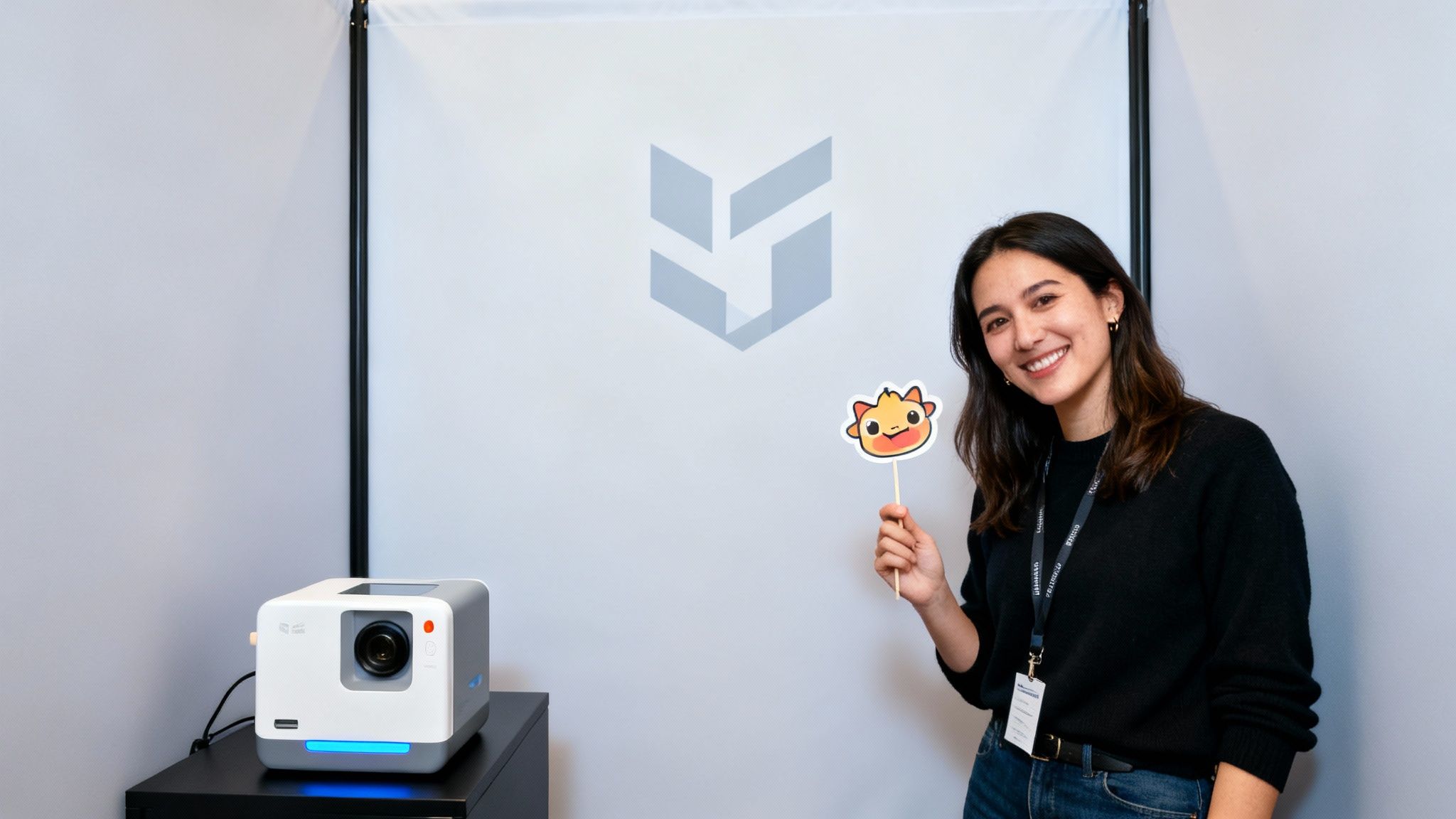 A smiling woman holds a cute cartoon character cutout next to a projector and a logo backdrop.