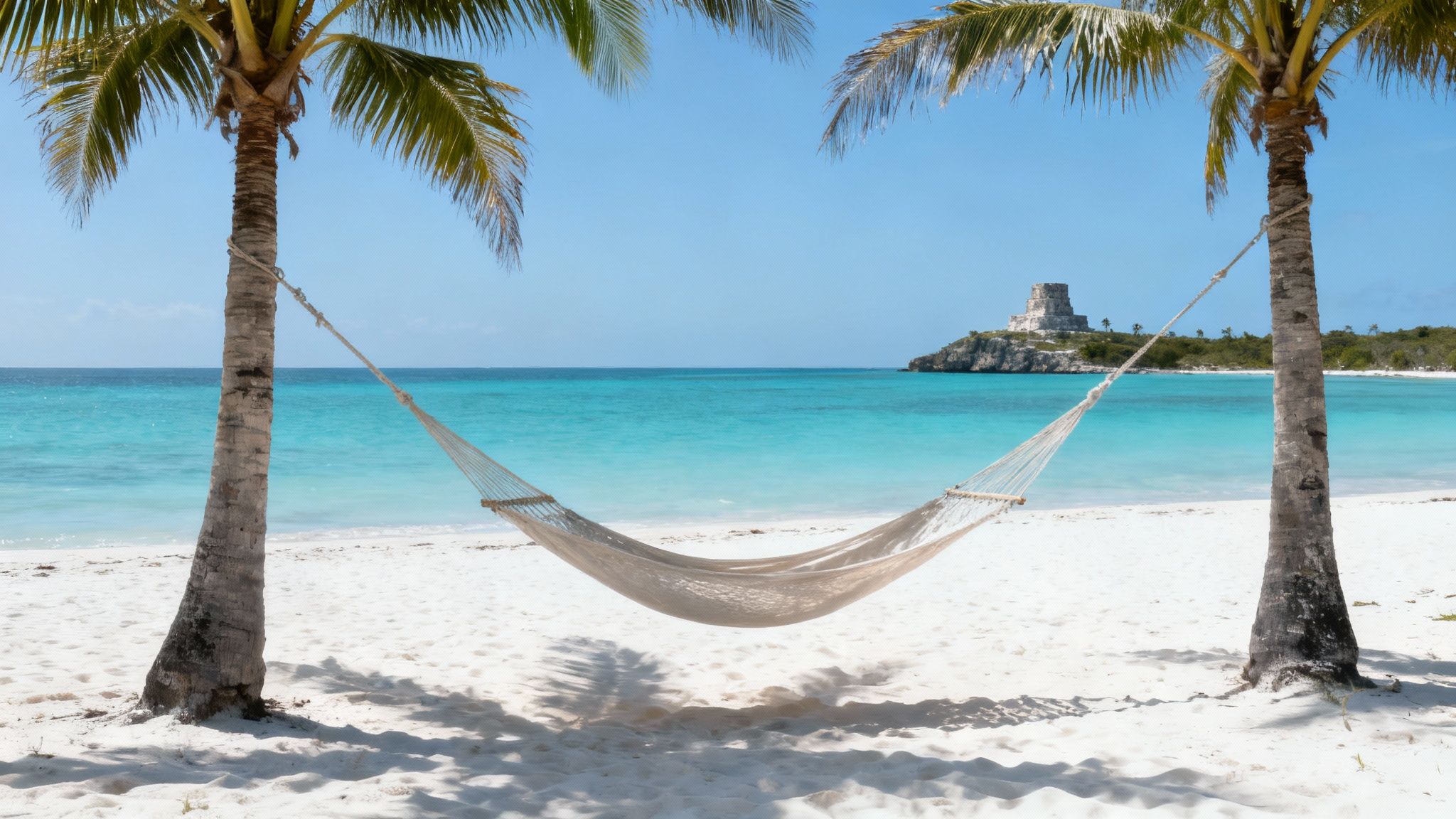 A scenic white sand beach with a hammock strung between two palm trees, overlooking turquoise waters and ancient ruins.