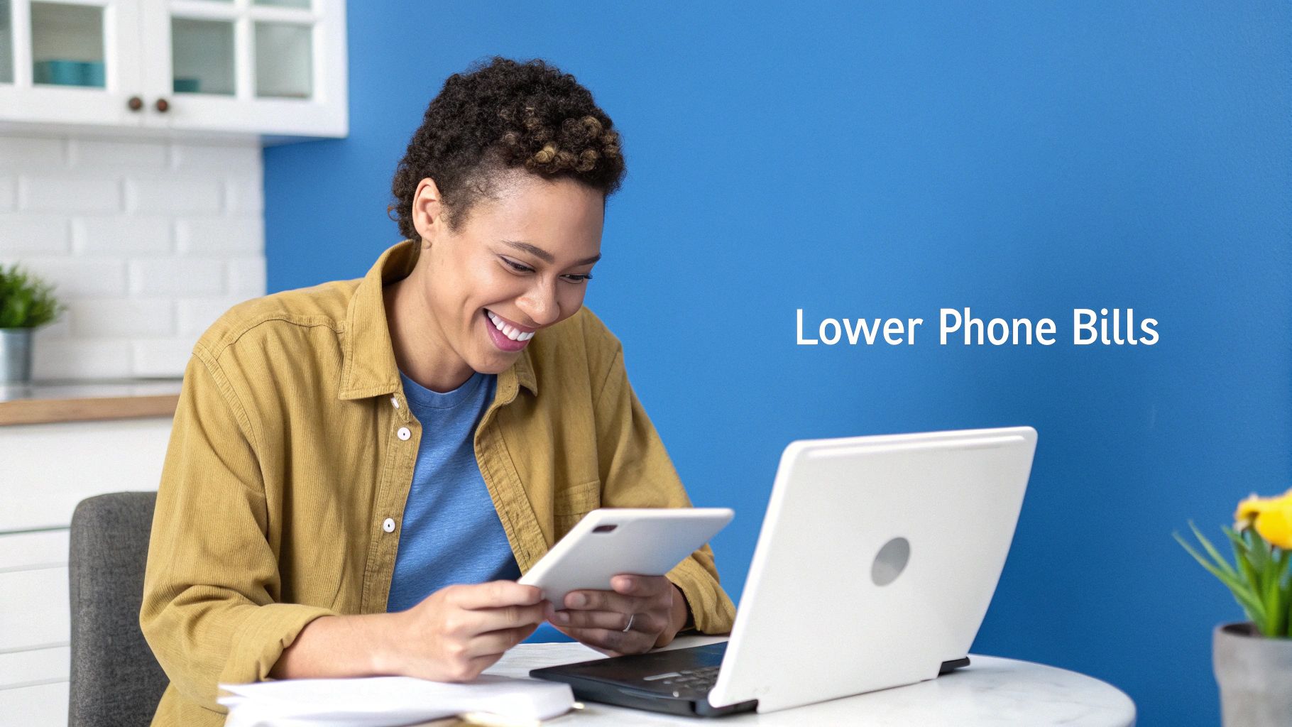 A smiling woman uses a tablet and laptop, happy about lower phone bills at home.