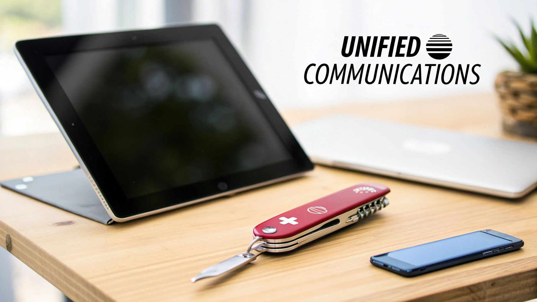 A modern workspace with a tablet, laptop, smartphone, and a Swiss Army knife on a wooden desk, emphasizing unified communications.
