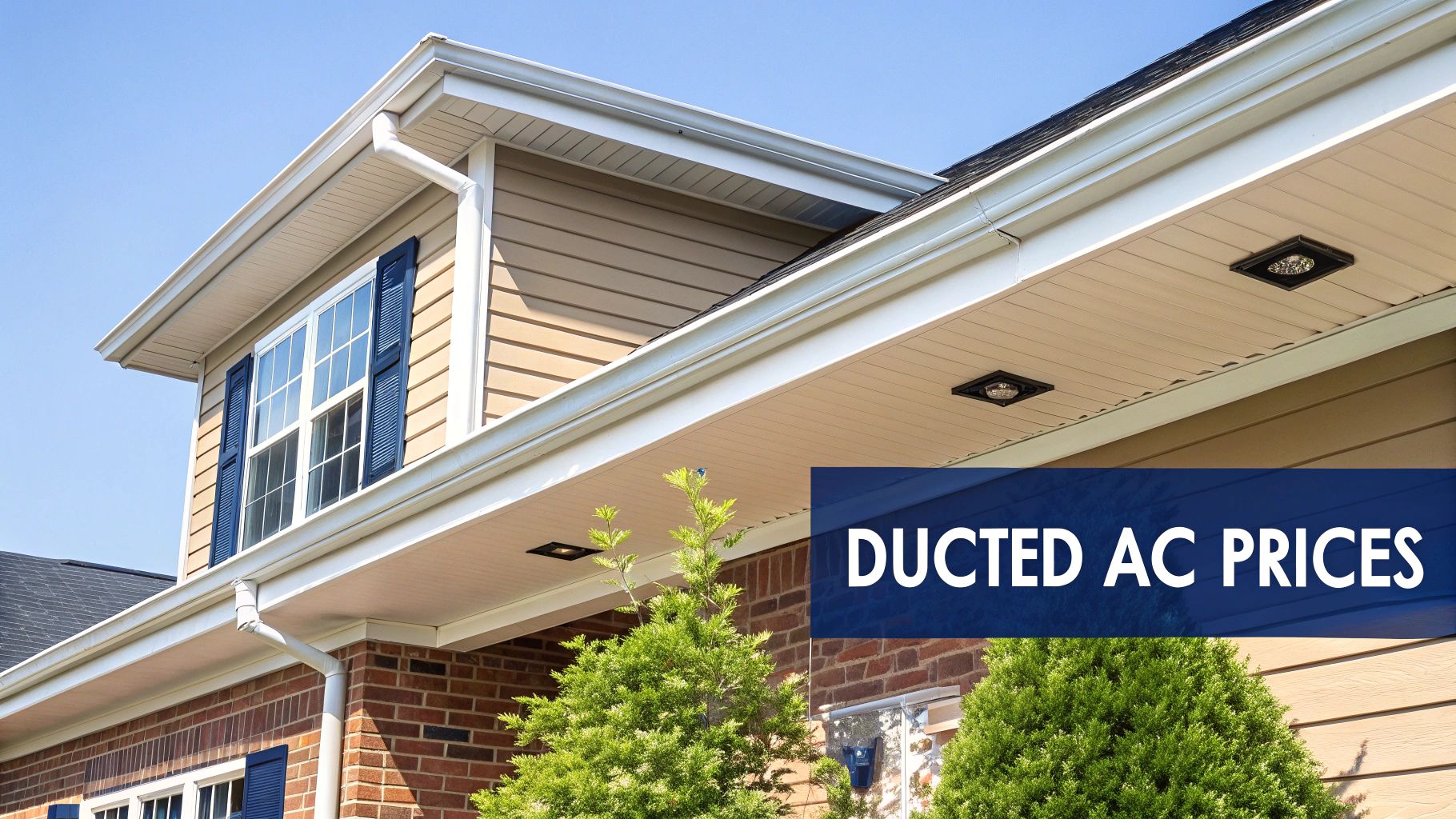 A house exterior with tan siding, brick facade, white gutters, and a dormer with blue shutters under a clear sky.