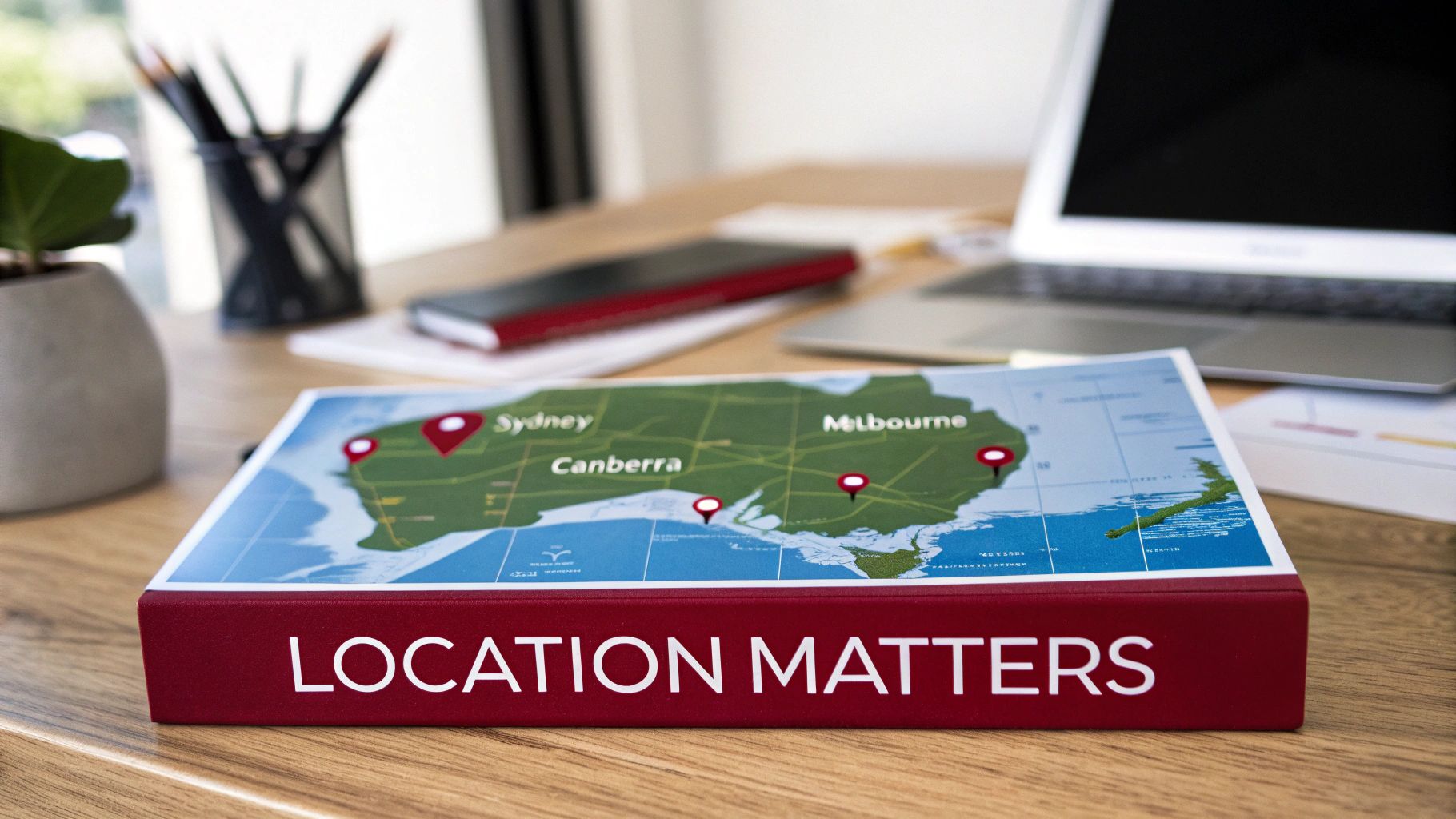 A red book titled "LOCATION MATTERS" with a map of Australia showing cities like Sydney and Melbourne on a wooden desk.