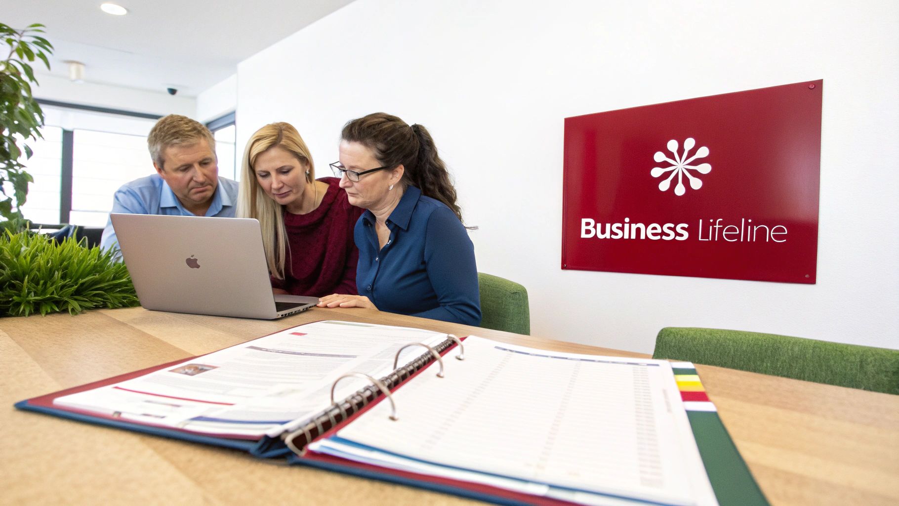Three business professionals collaborating around a laptop in a bright office meeting room.