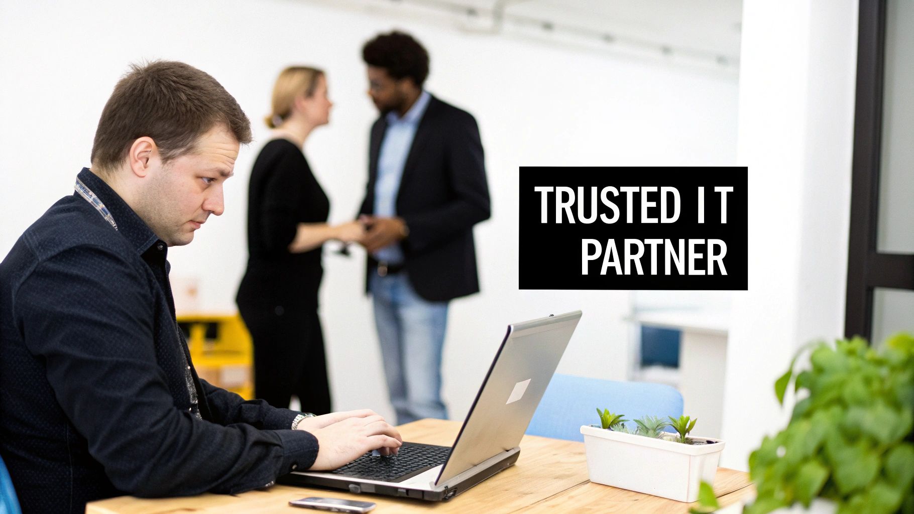 A man works diligently on a laptop at a desk, with "TRUSTED IT PARTNER" text overlay.