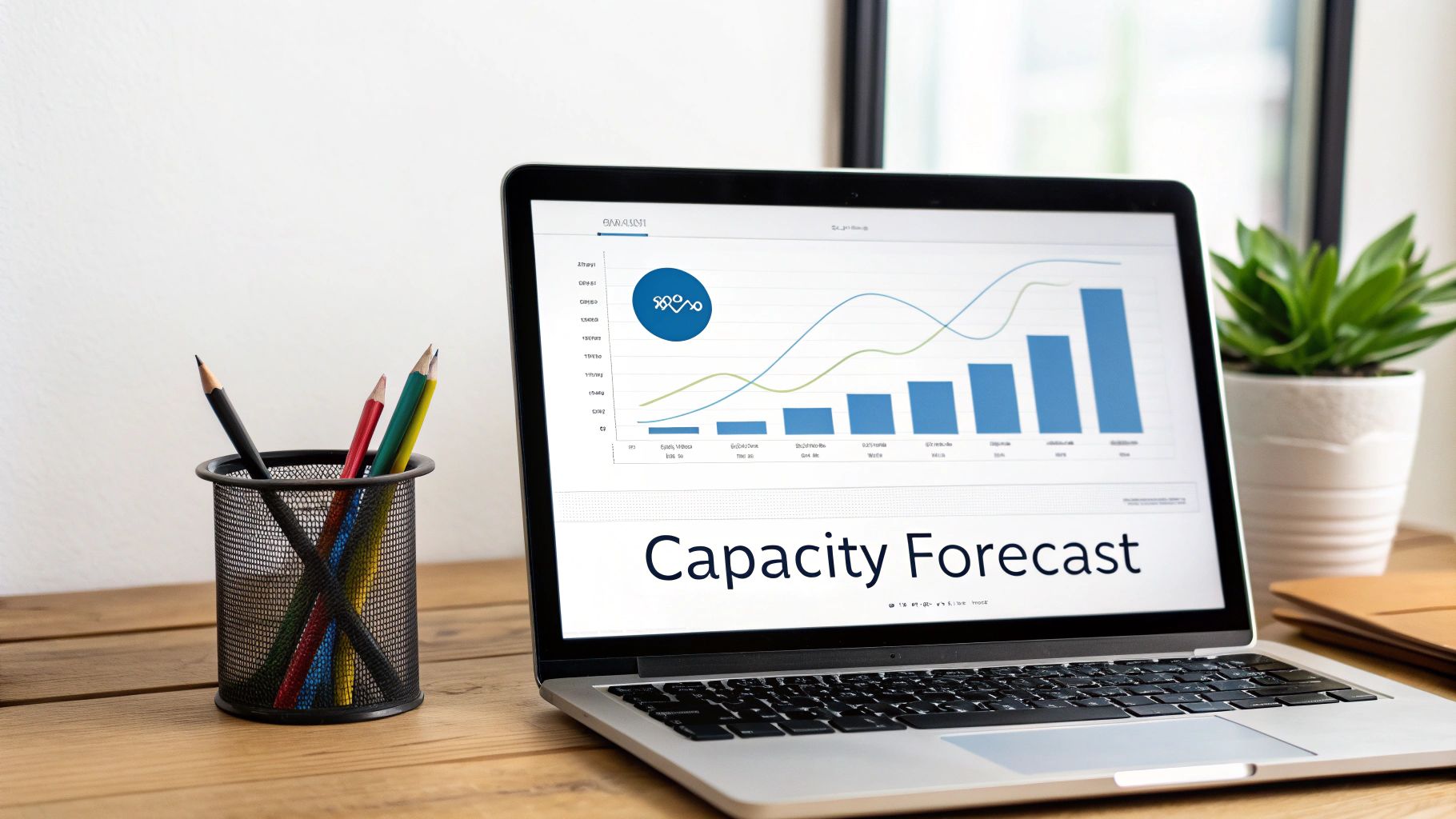 A laptop displaying a capacity forecast chart on a wooden desk with pencils and a plant.
