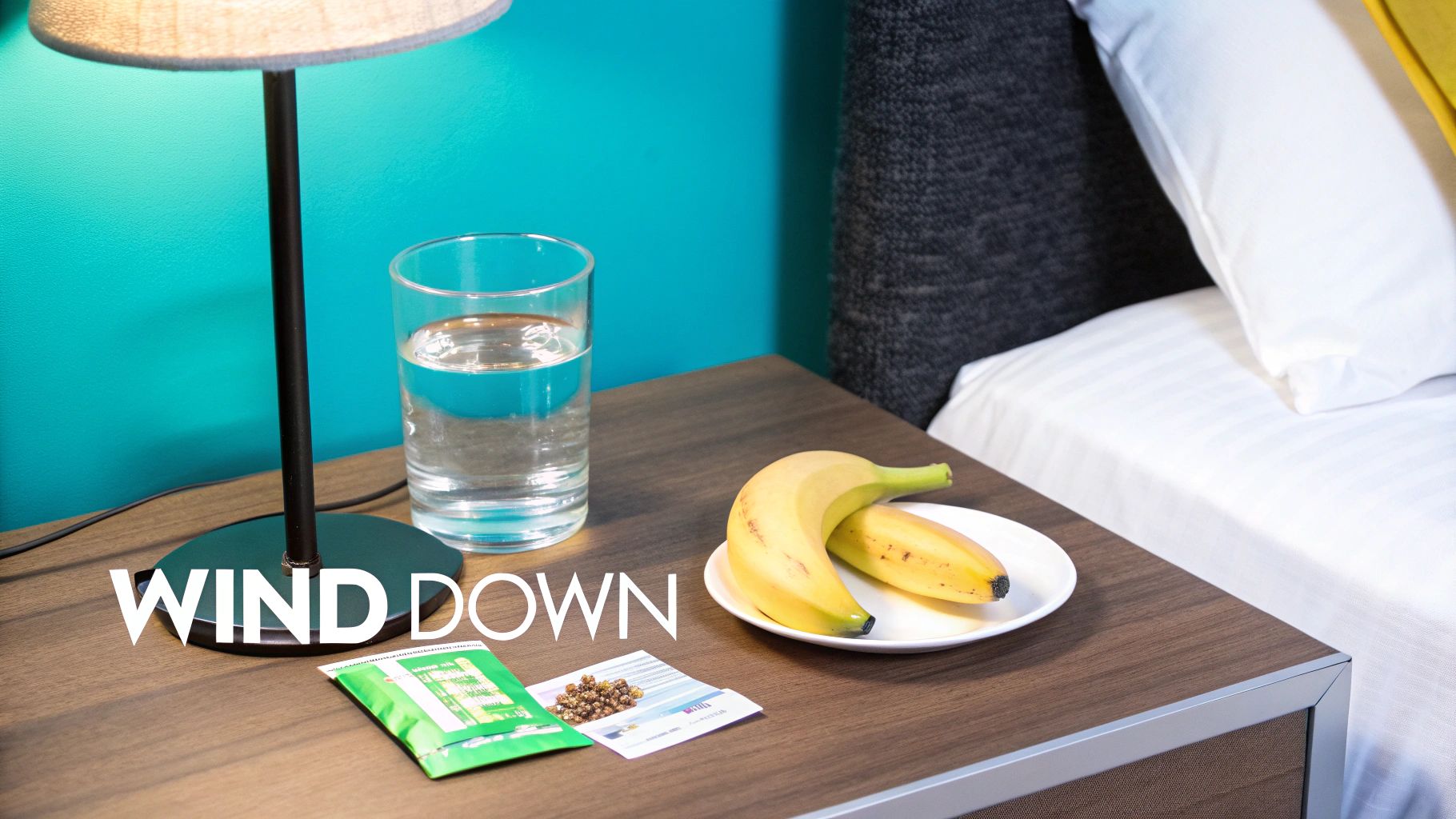 A bedside table with a glowing lamp, glass of water, bananas, and sachets, ready for winding down.