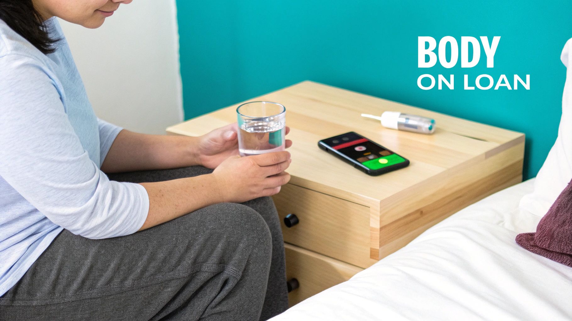 Person holding a glass of water next to a smartphone and a medical device on a nightstand.