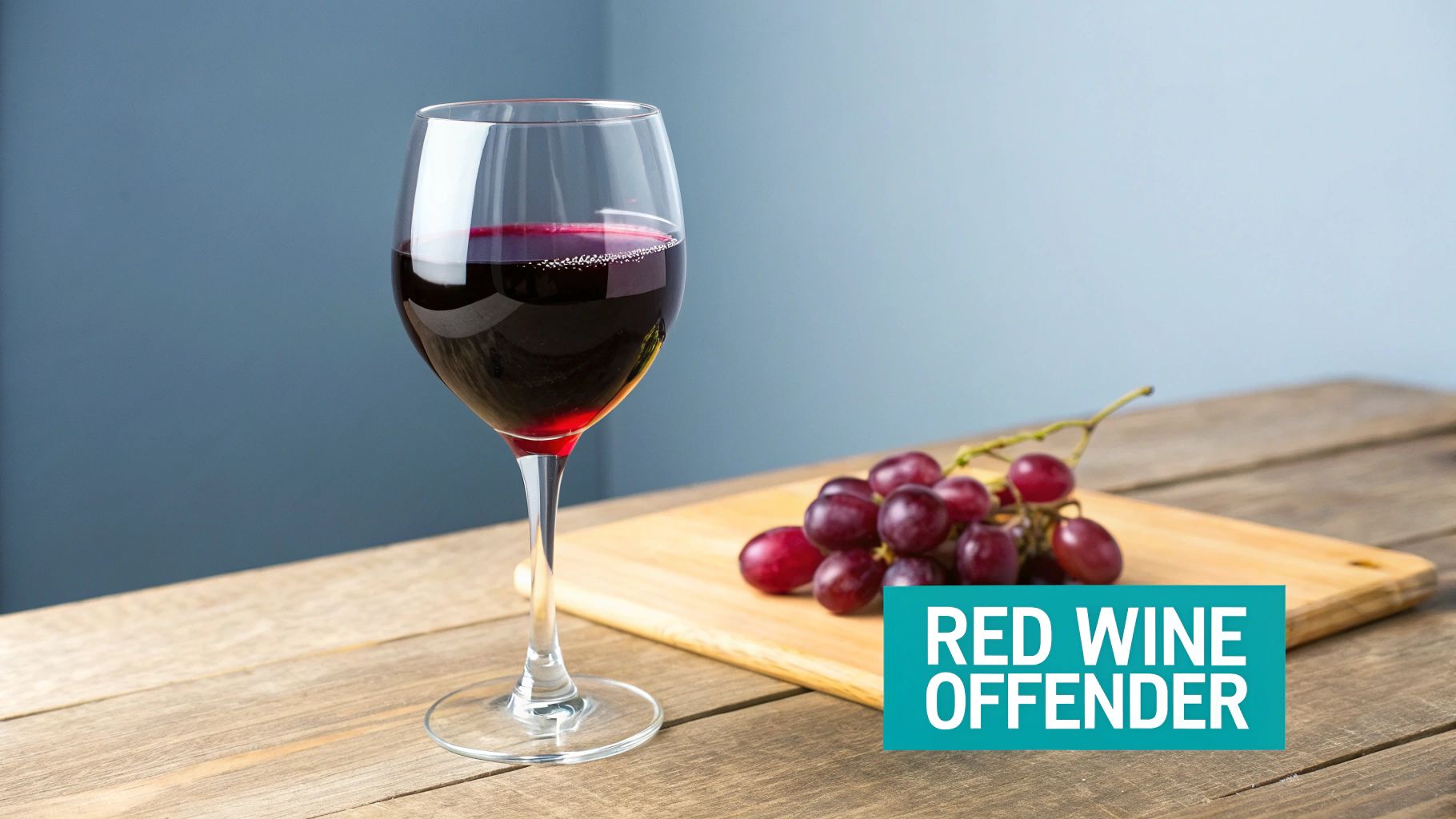 A glass of red wine and a bunch of red grapes on a wooden table, with text 'RED WINE OFFENDER'.