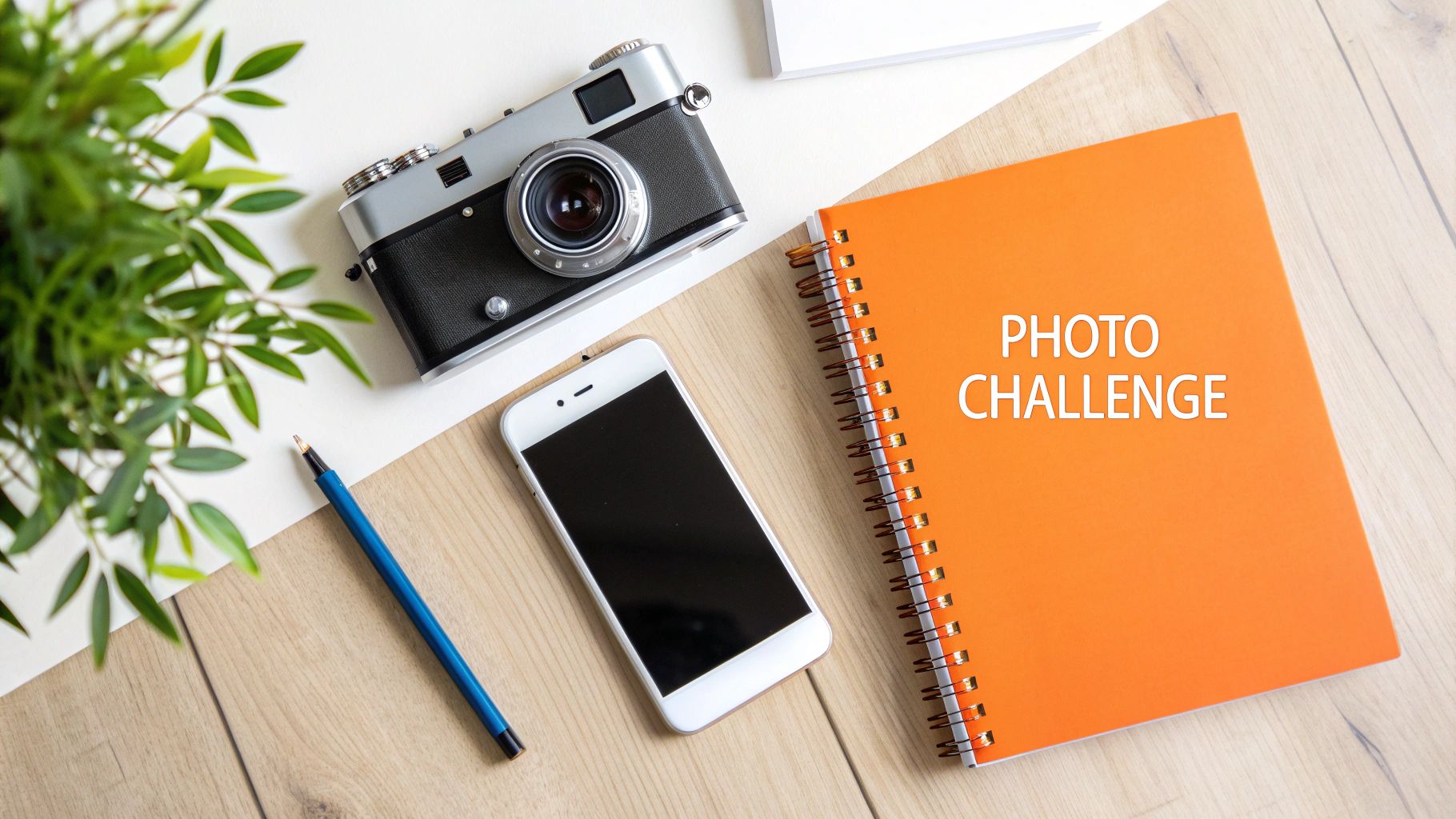 Flat lay with vintage camera, smartphone, pen, plant, and a notebook stating 'PHOTO CHALLENGE' on wood and white.