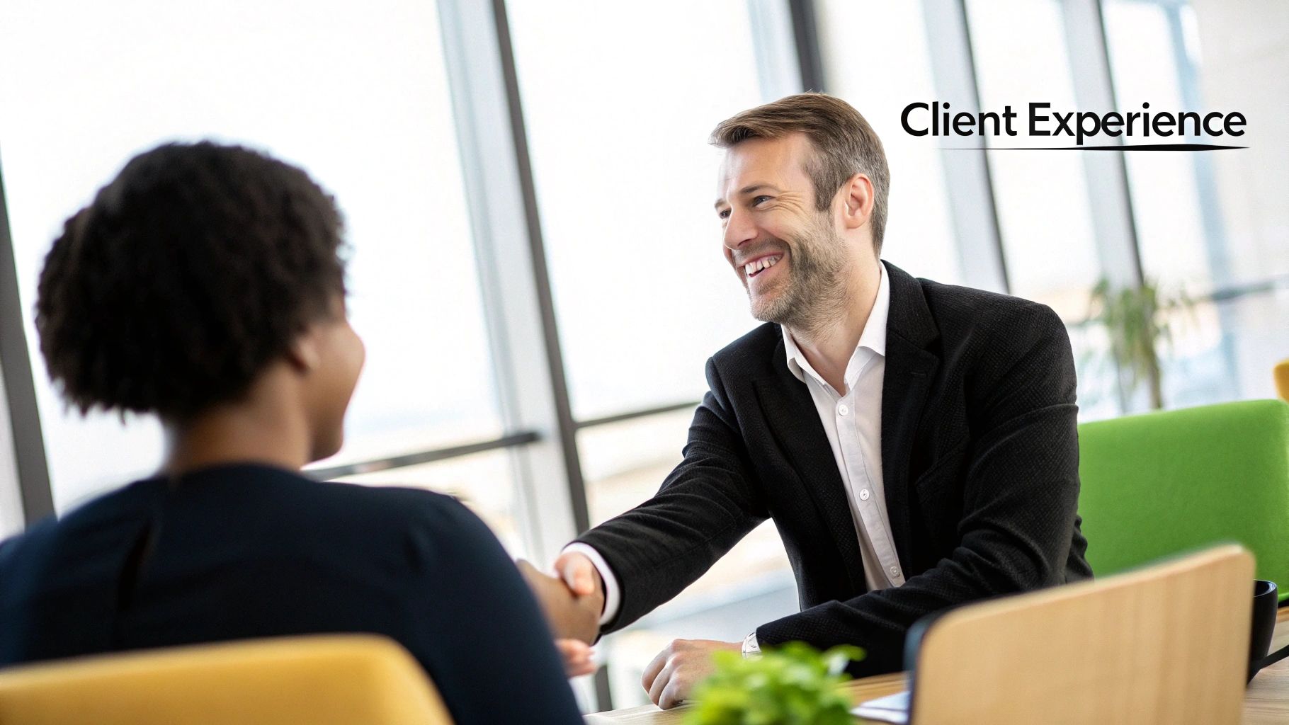 Two people shaking hands across a desk in a modern office, signifying a successful client partnership and positive experience.