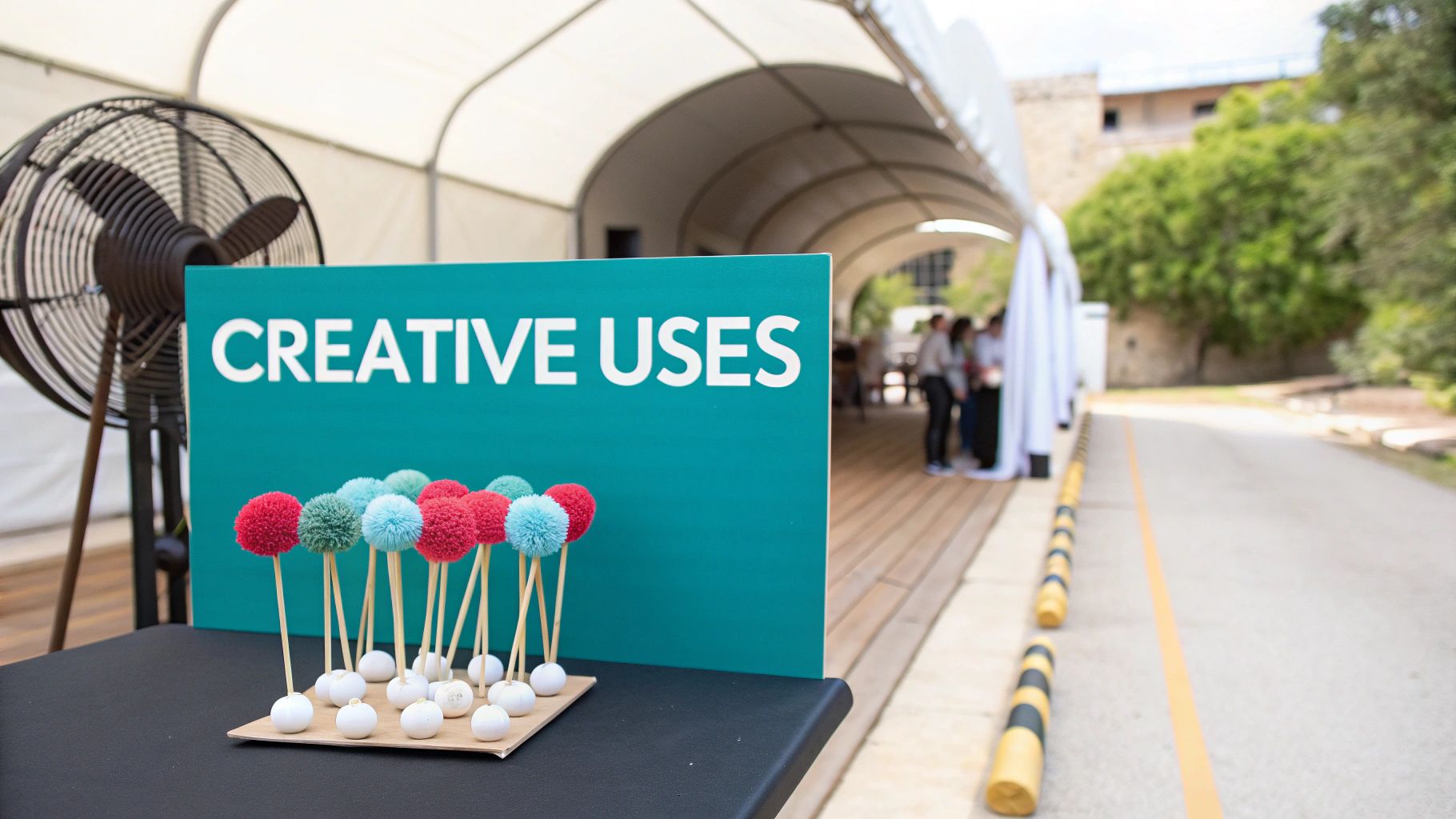 Colorful pom-poms on sticks in front of a teal "CREATIVE USES" sign at an outdoor event.