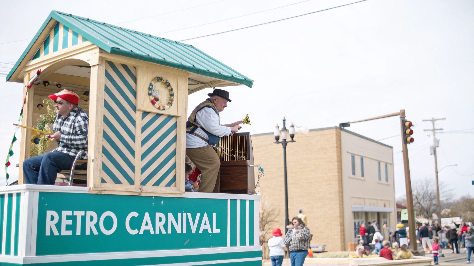 Two men on a 'Retro Carnival' parade float, one playing a wind-up organ.