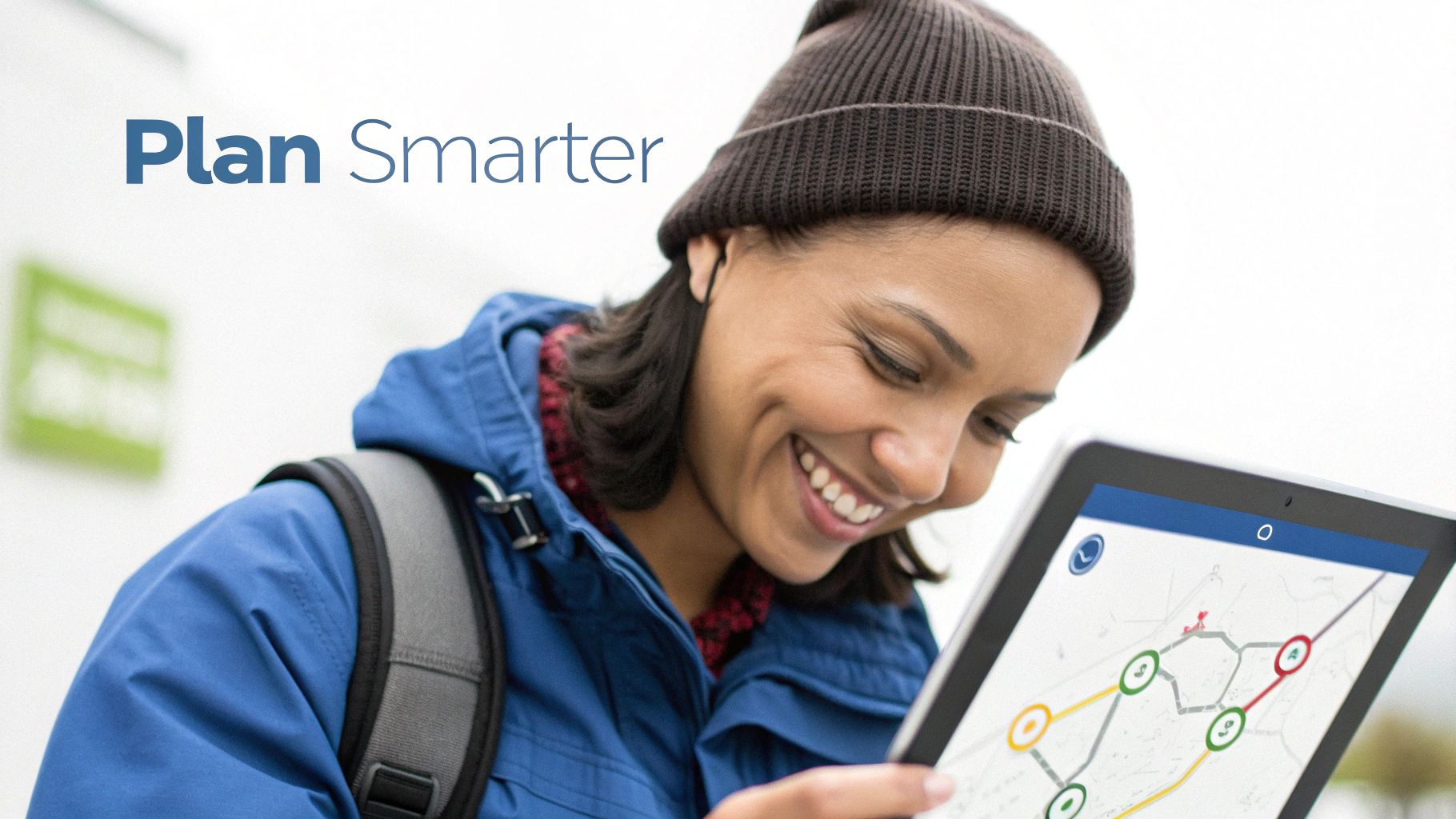 A smiling woman in a beanie and jacket views a map on a tablet, planning routes.