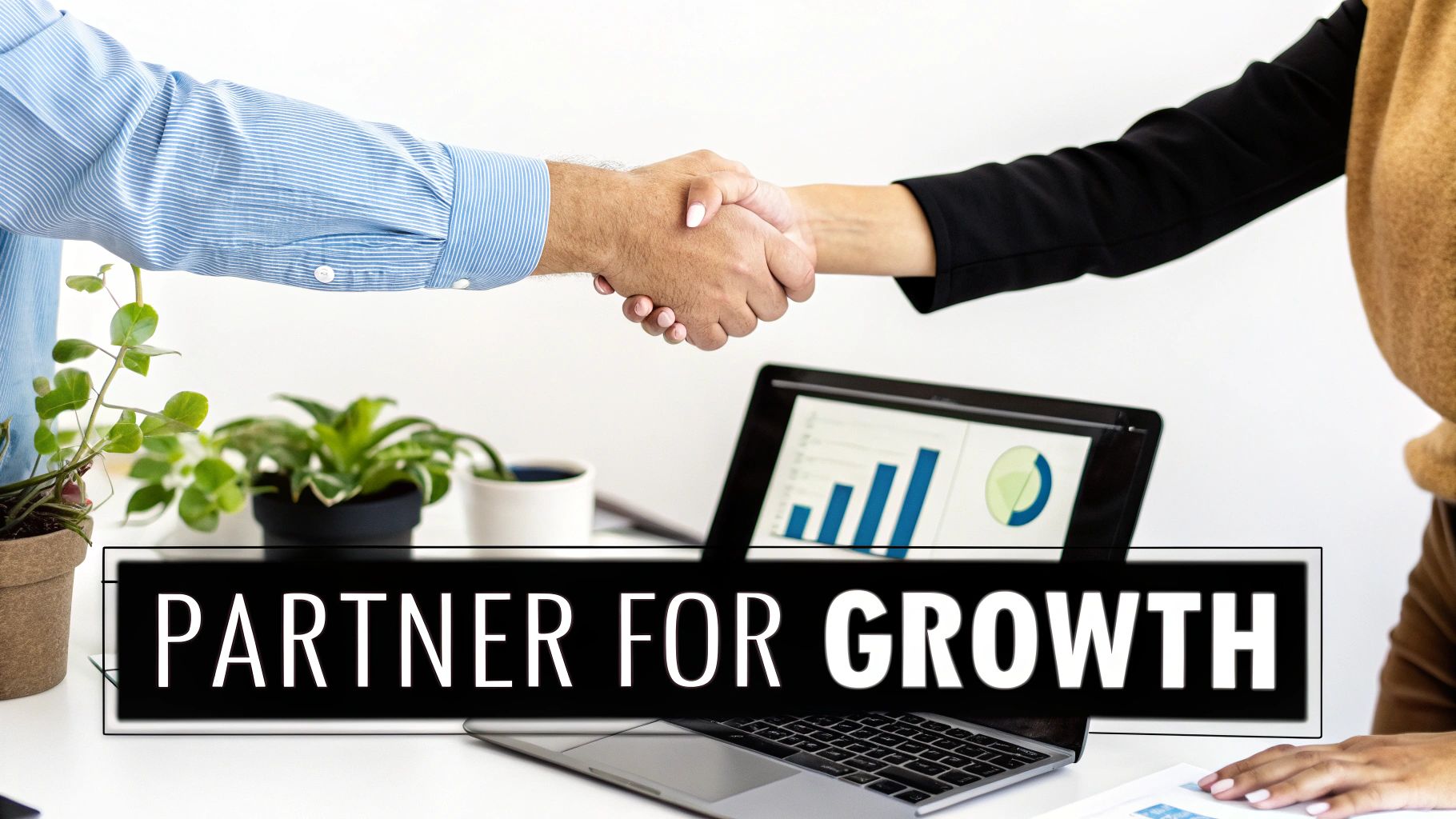 Business partners shaking hands over a desk with charts on a laptop, emphasizing growth.