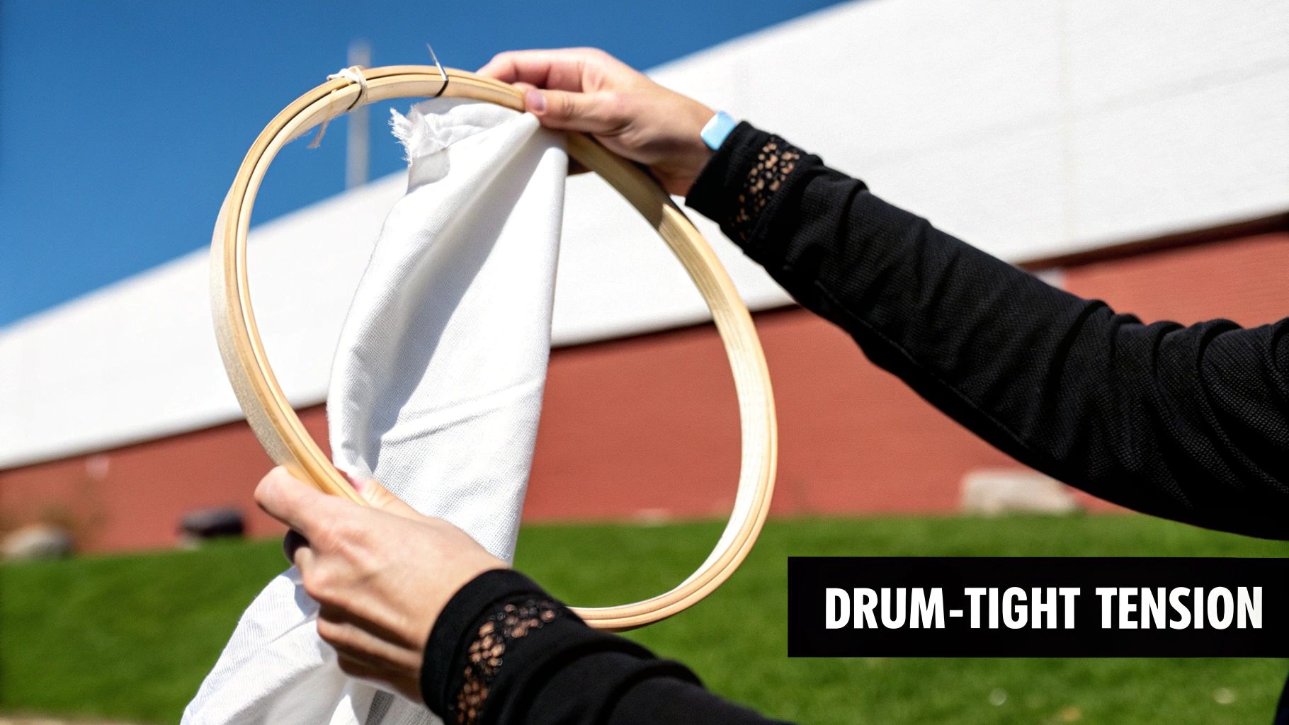 Close-up of hands holding a wooden embroidery hoop with white fabric stretched tight under a blue sky.