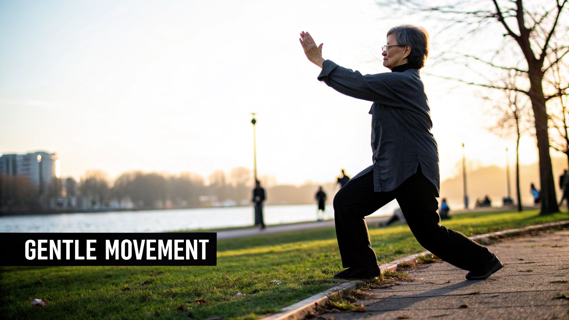 An older woman practices gentle Tai Chi or Qigong movements outdoors by a lake at sunset.