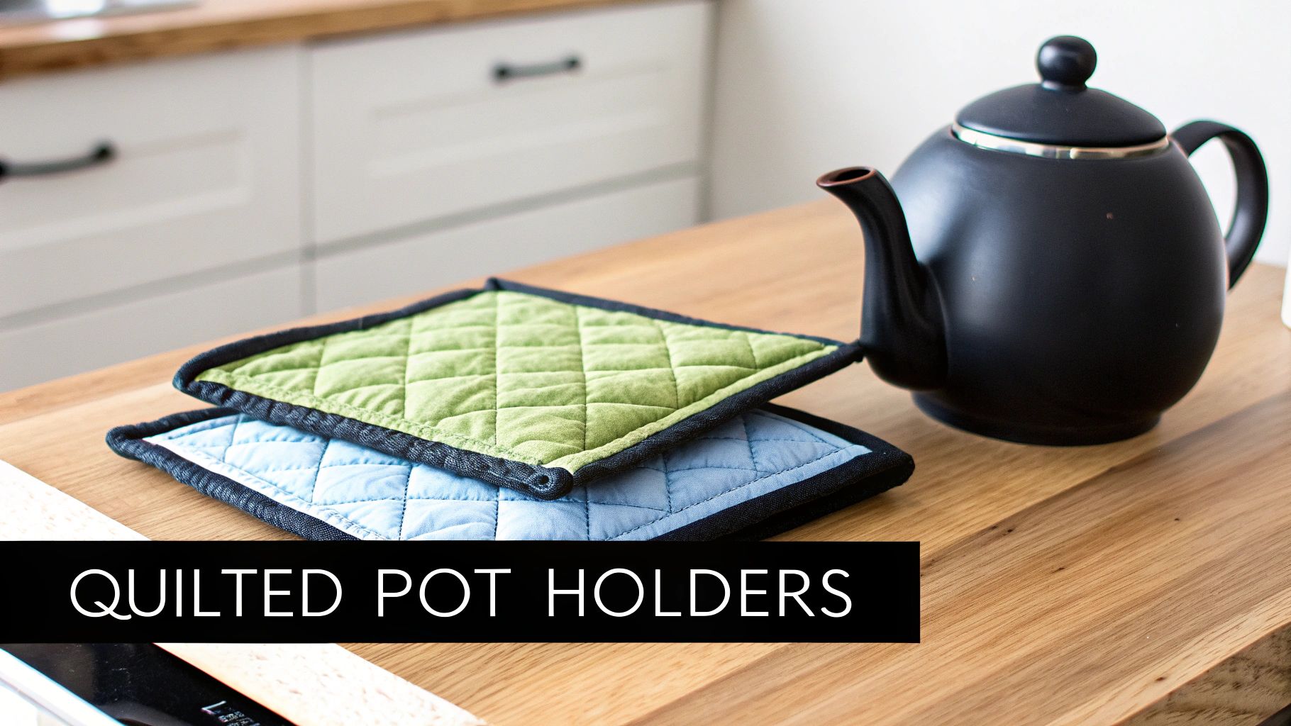 Two colorful quilted pot holders, one green and one blue, stacked next to a black teapot on a wooden kitchen counter.