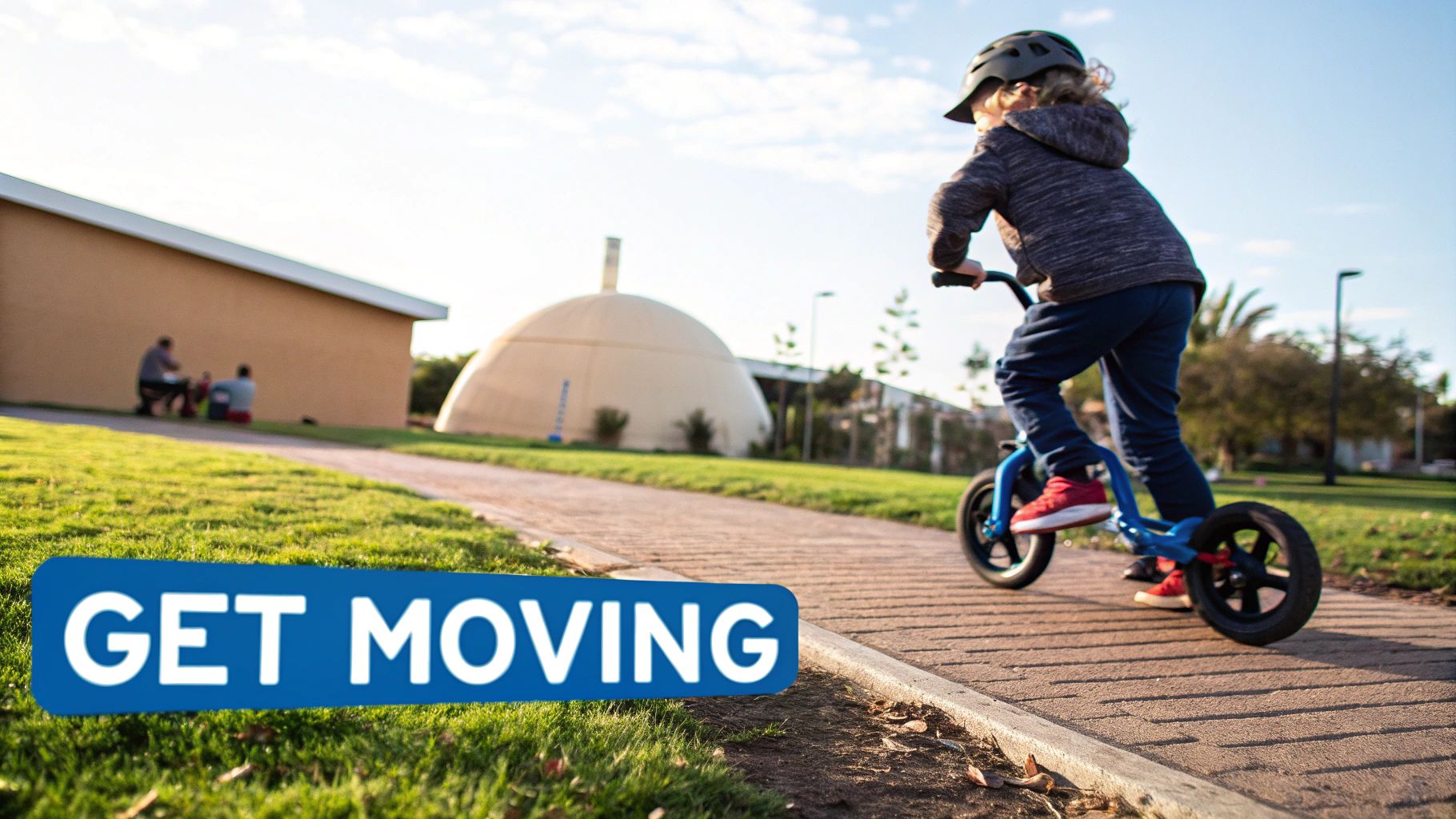 A young child wearing a helmet rides a blue balance bike on a path outdoors, with a "GET MOVING" banner.