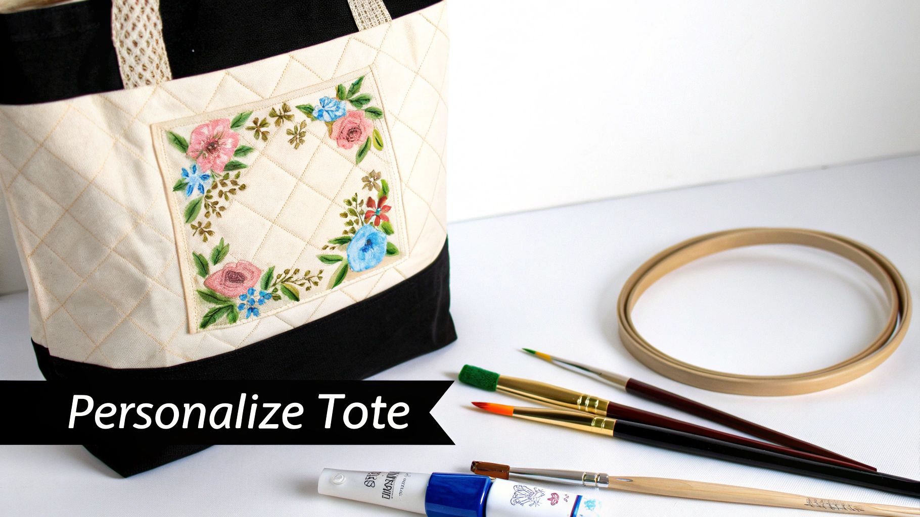 A quilted canvas tote bag with colorful floral embroidery, accompanied by paintbrushes and an embroidery hoop.