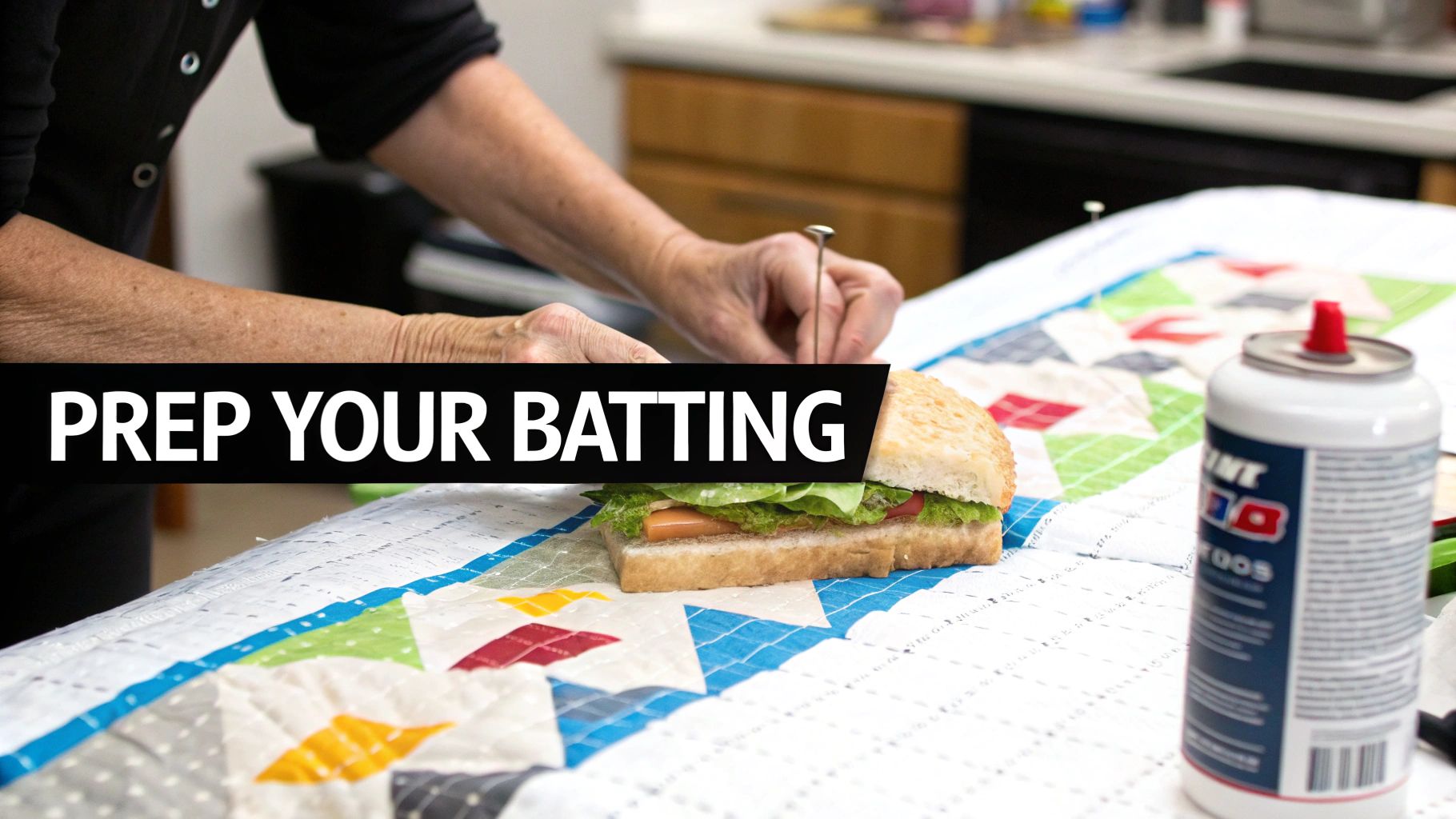 Hands preparing quilt batting on a colorful patchwork quilt, with a sandwich and spray can.